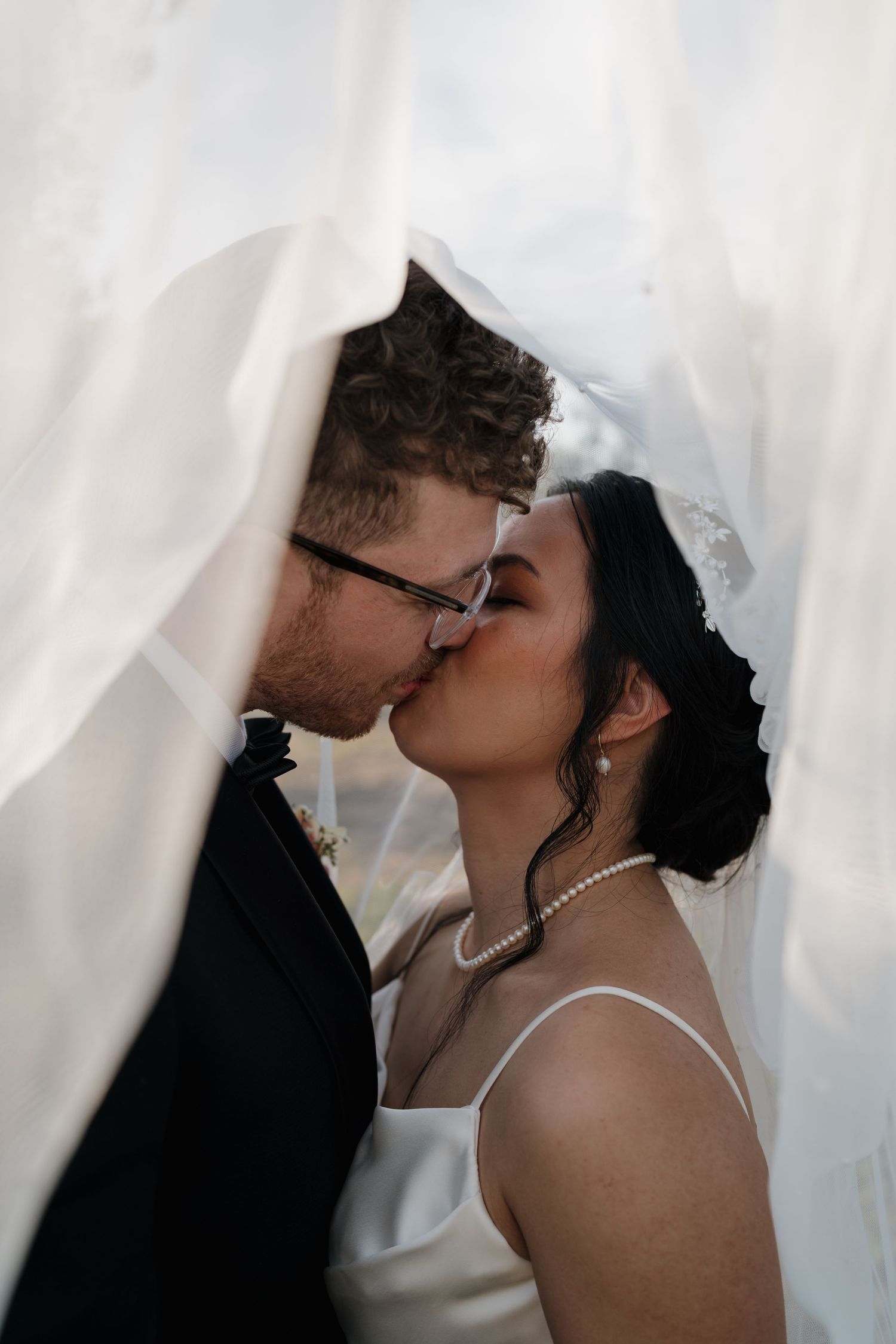 Romantic wedding couple sharing an intimate kiss against a white backdrop.