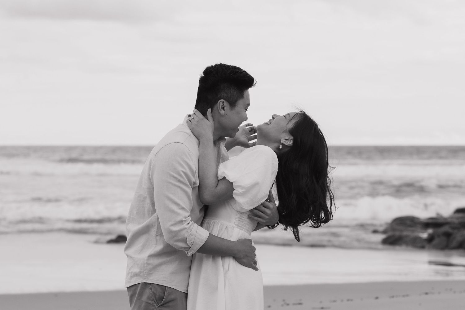 Romantic couple sharing an intimate moment on a rocky beach at sunset.
