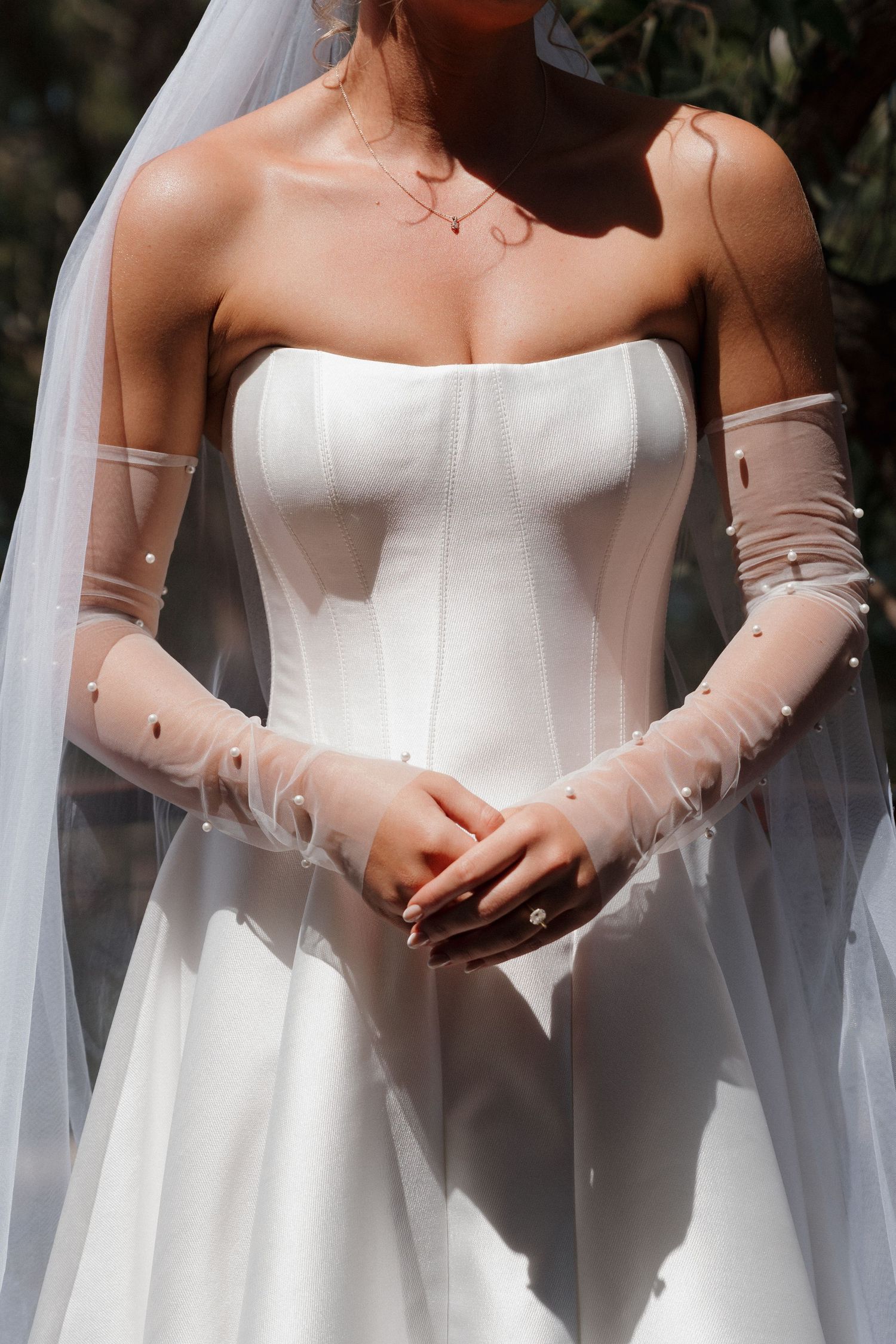 Row of elegant white wedding dresses with sheer sleeves and veils.