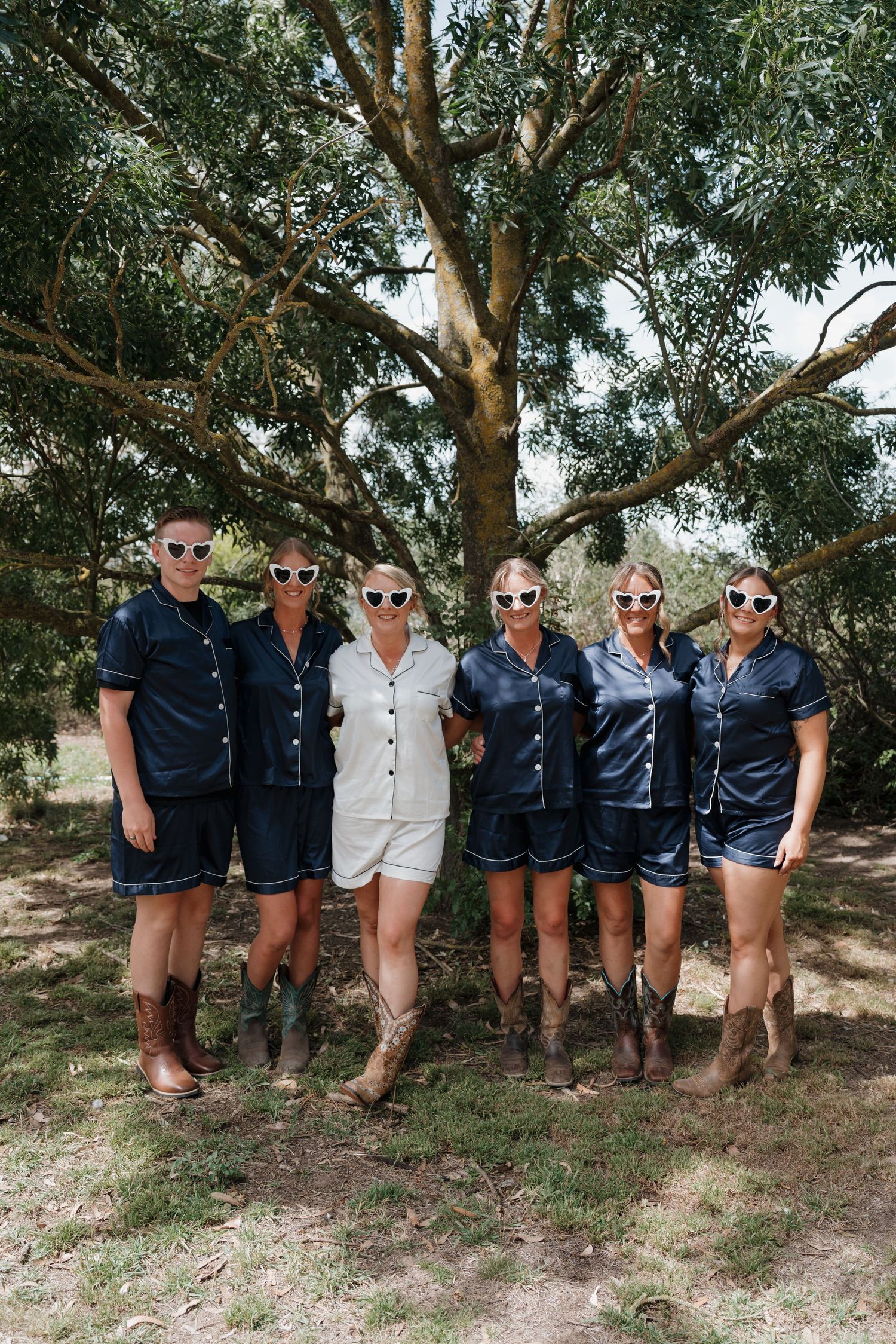 Wedding party wearing navy and white outfits poses together under trees outdoors.