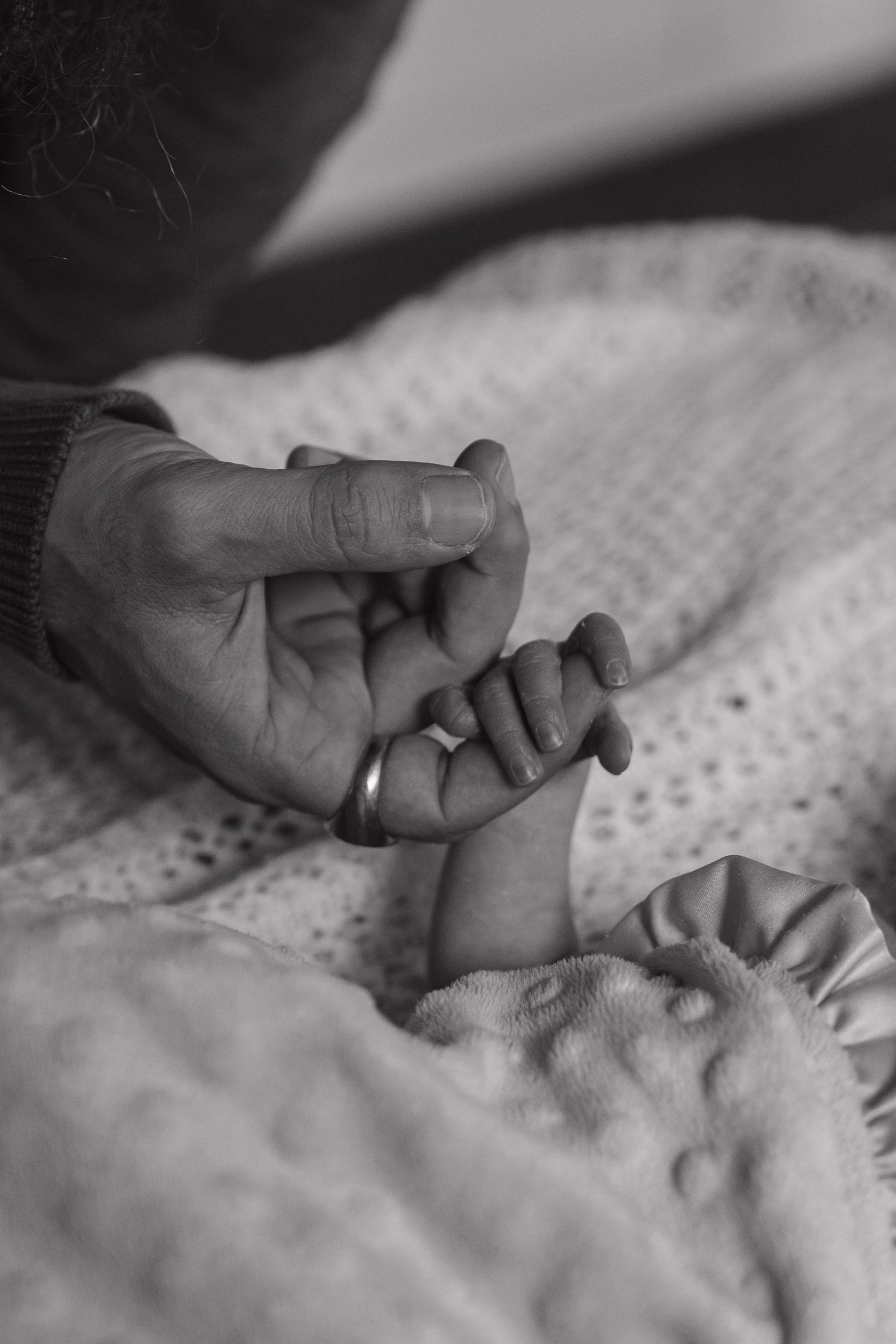 Tender black and white image of hands intertwined on textured fabric.