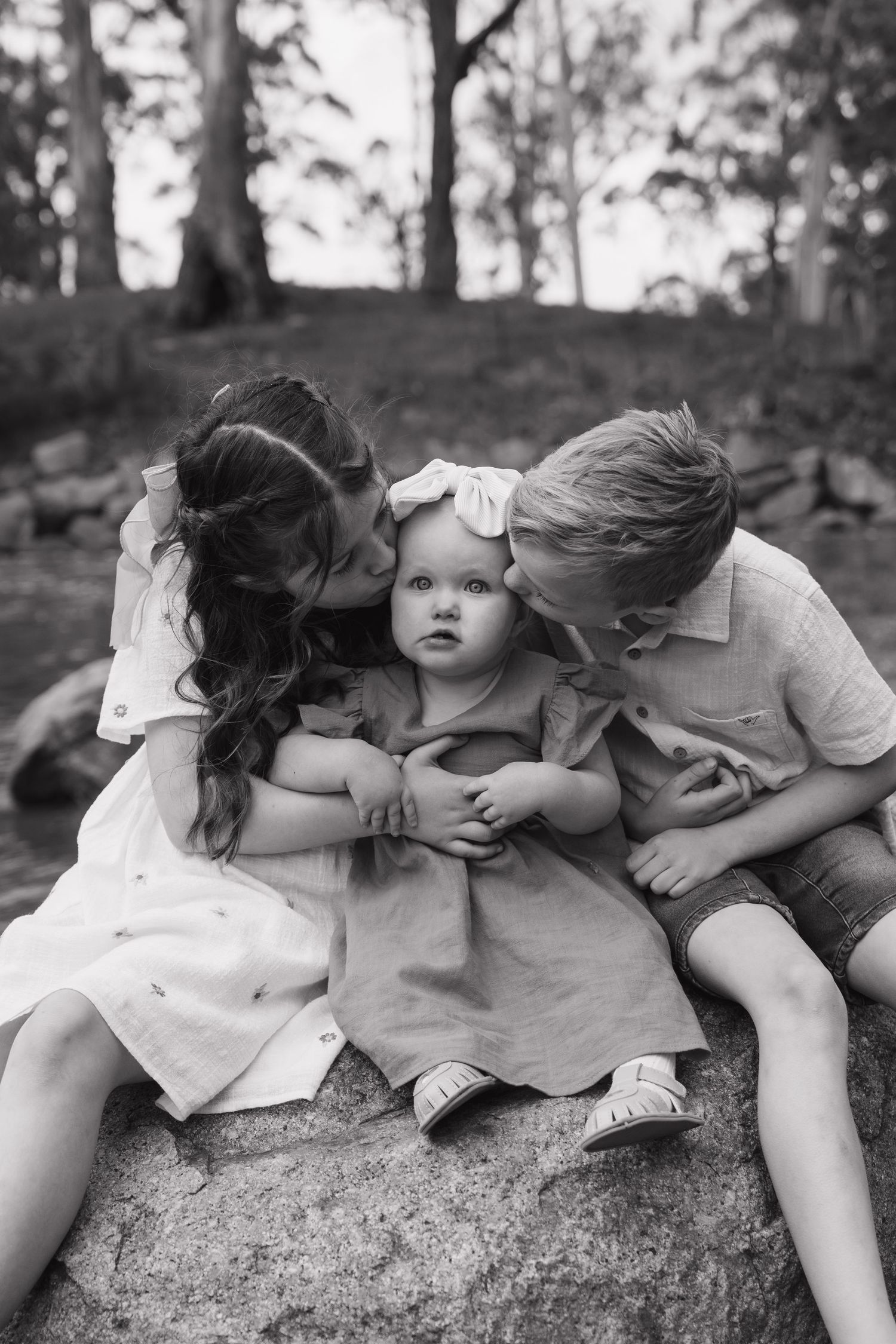 A tender black and white portrait of siblings sharing affectionate moments on a rock.