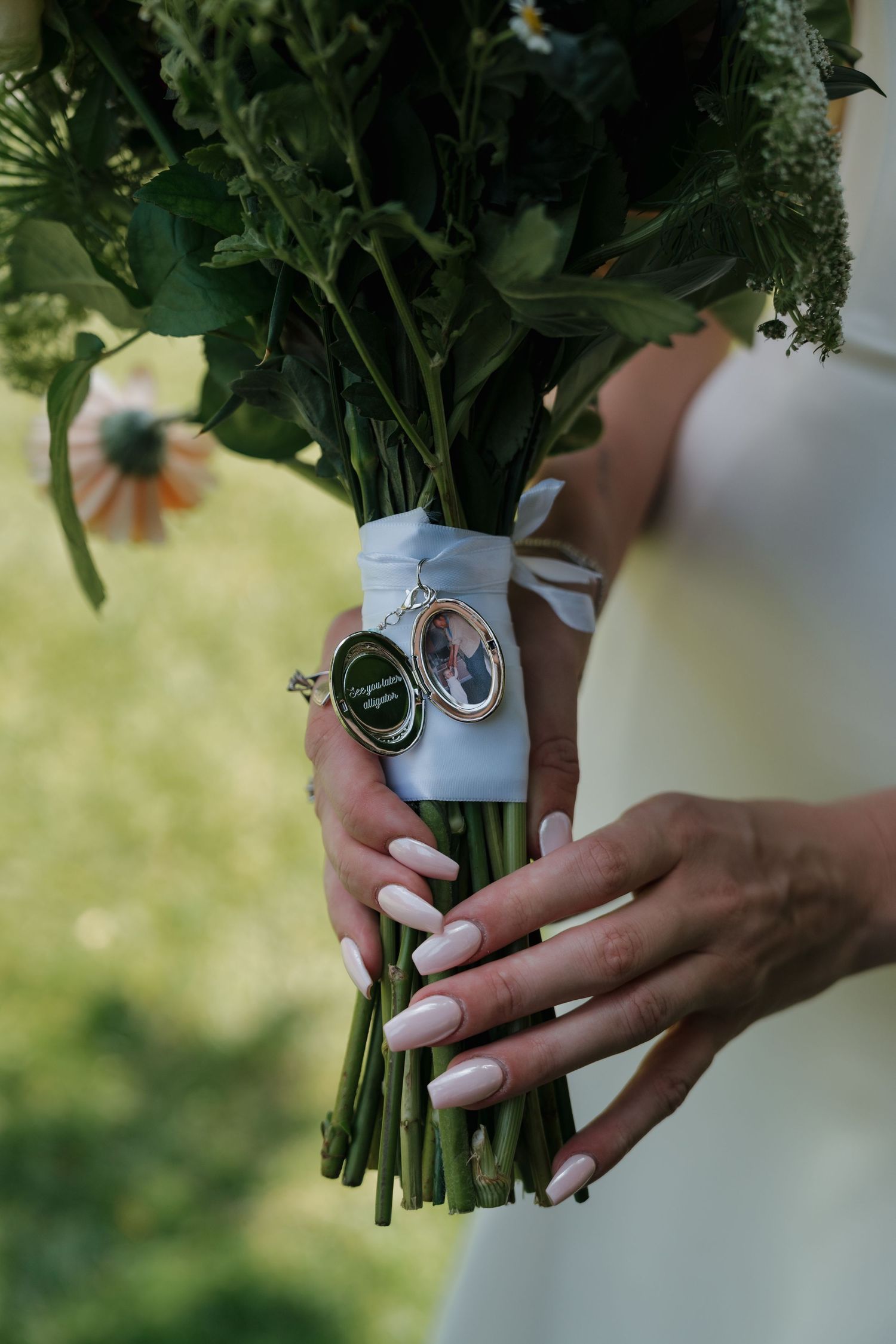 Close-up of hands holding a bridal bouquet wrapped with ribbon and memorial photo charms.