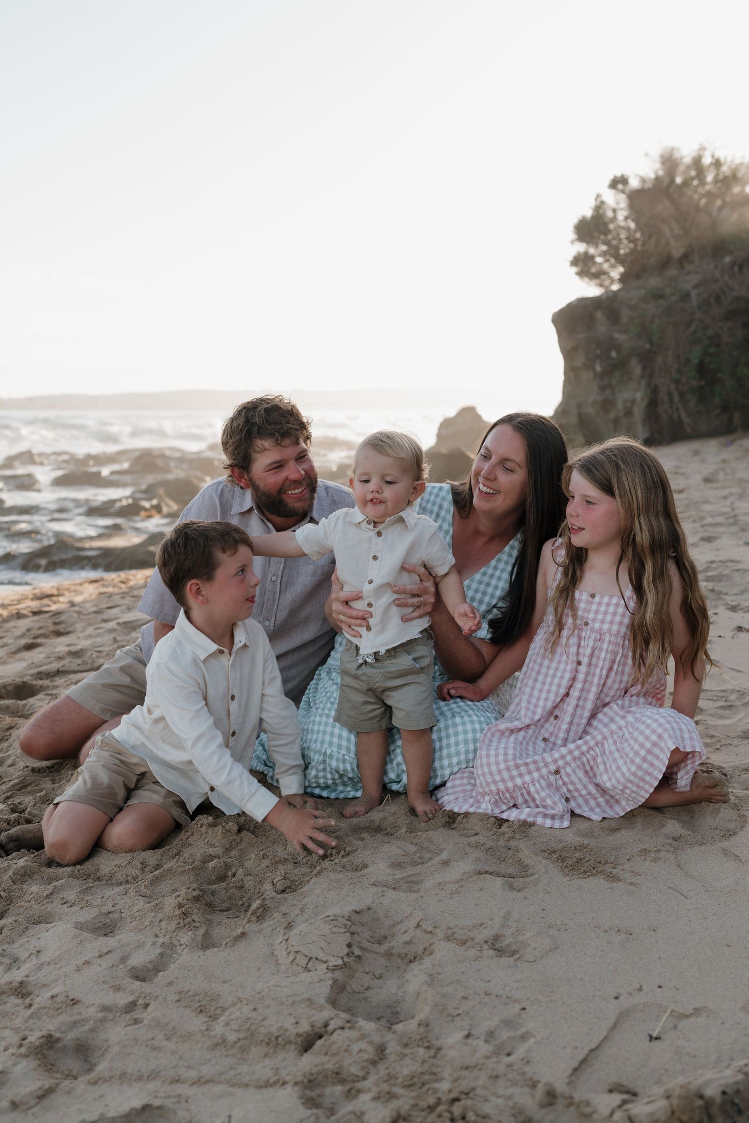 Family lying together on beach sand at sunset.