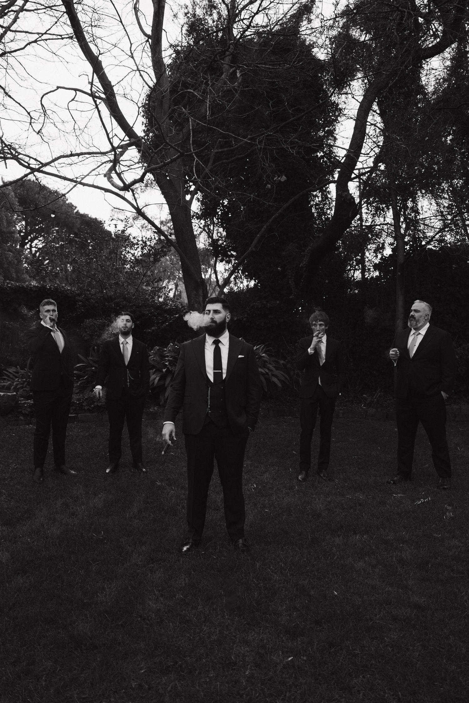 Group of people in dark formal attire standing outdoors against a moody sky.
