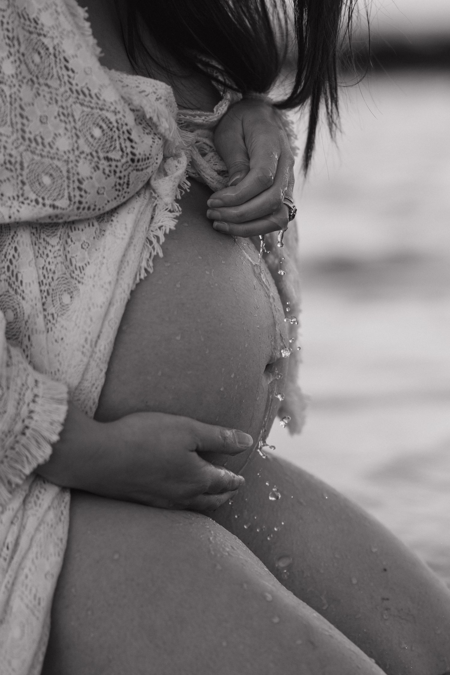 Close-up of pregnant belly with lace dress detail at the beach.