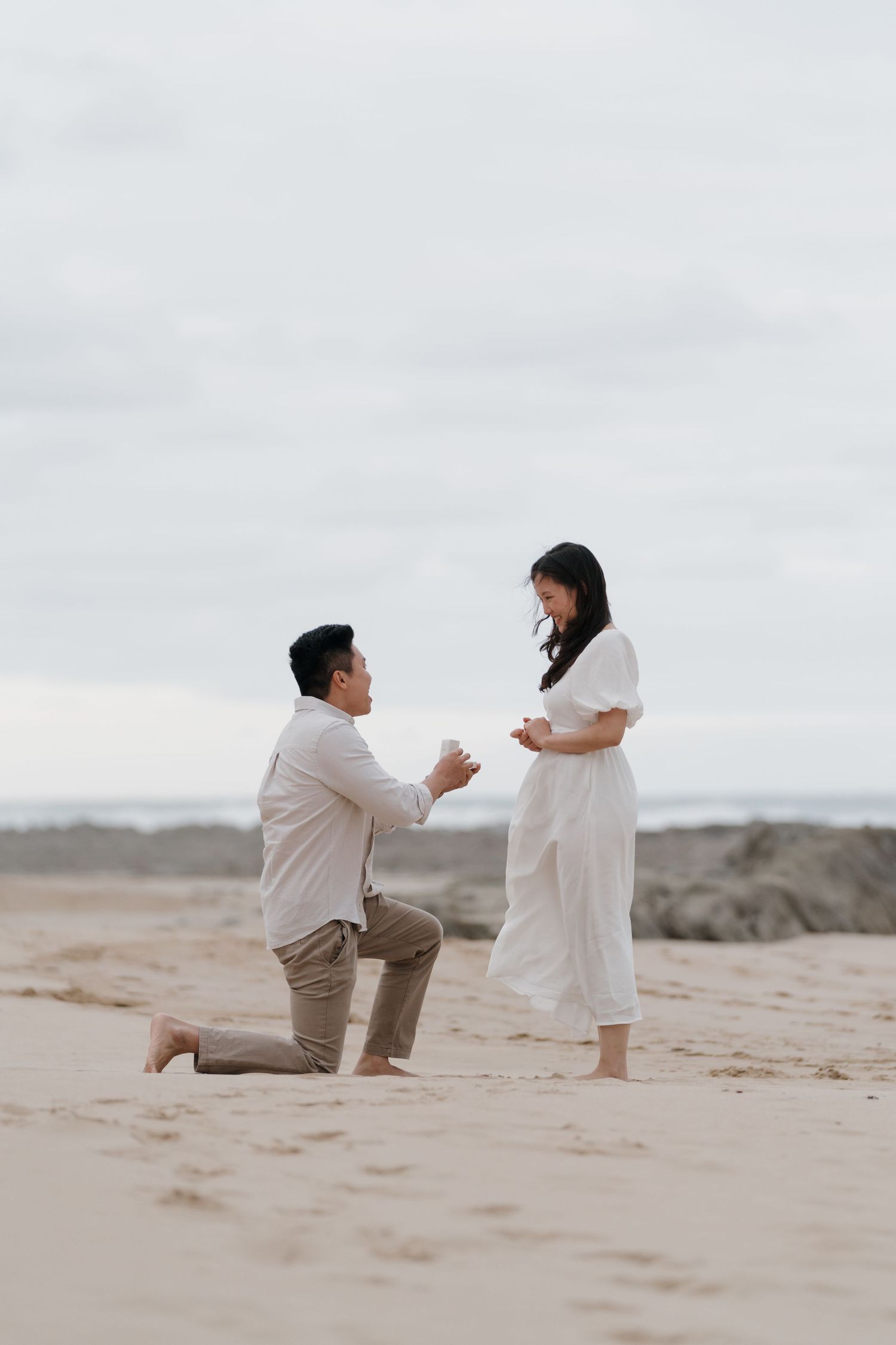 Marriage proposal scene on a sandy beach with dramatic coastal landscape.