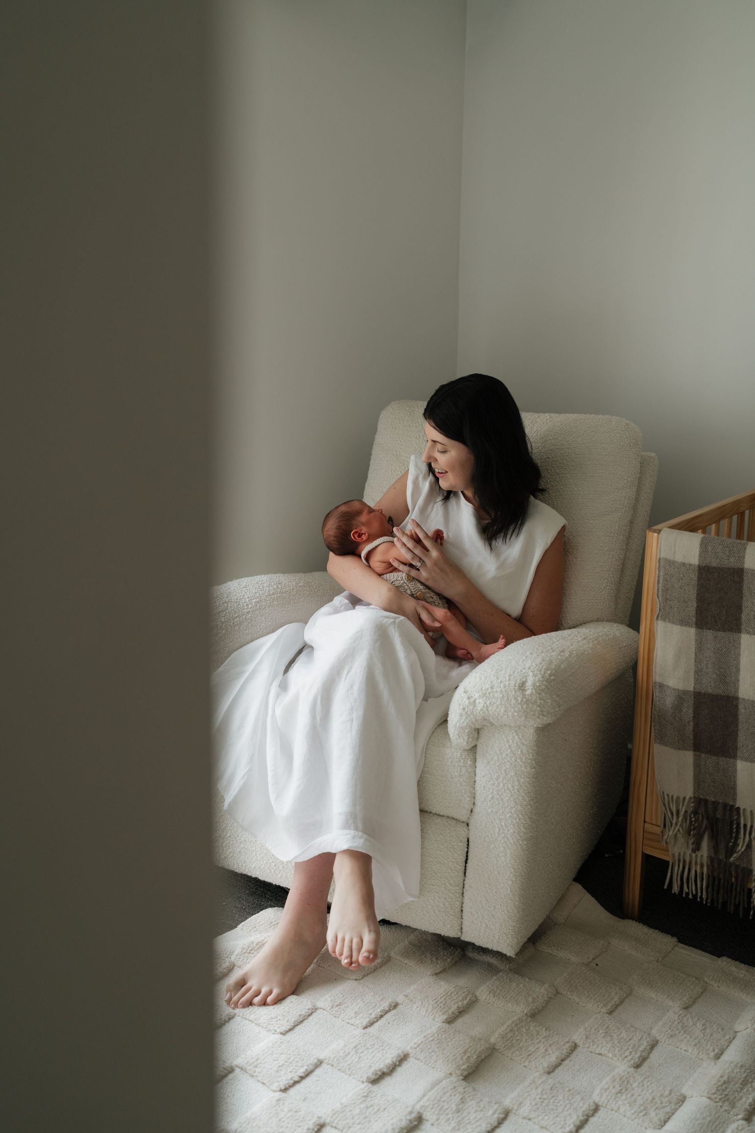 Parent in white dress holding baby in a minimalist nursery setting.