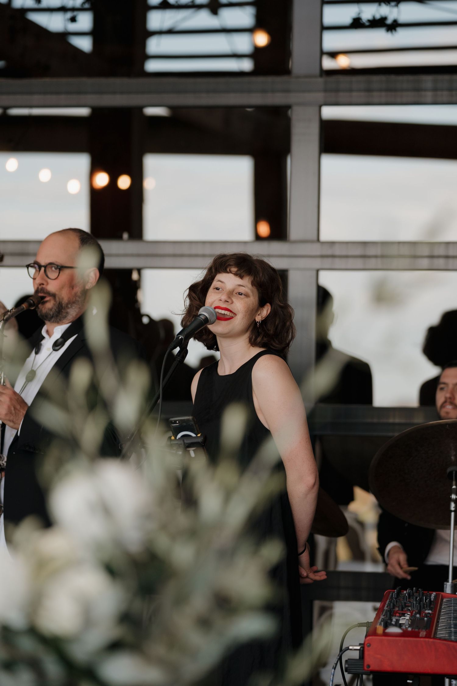 Musicians perform at an indoor wedding reception with string lights visible in the background.