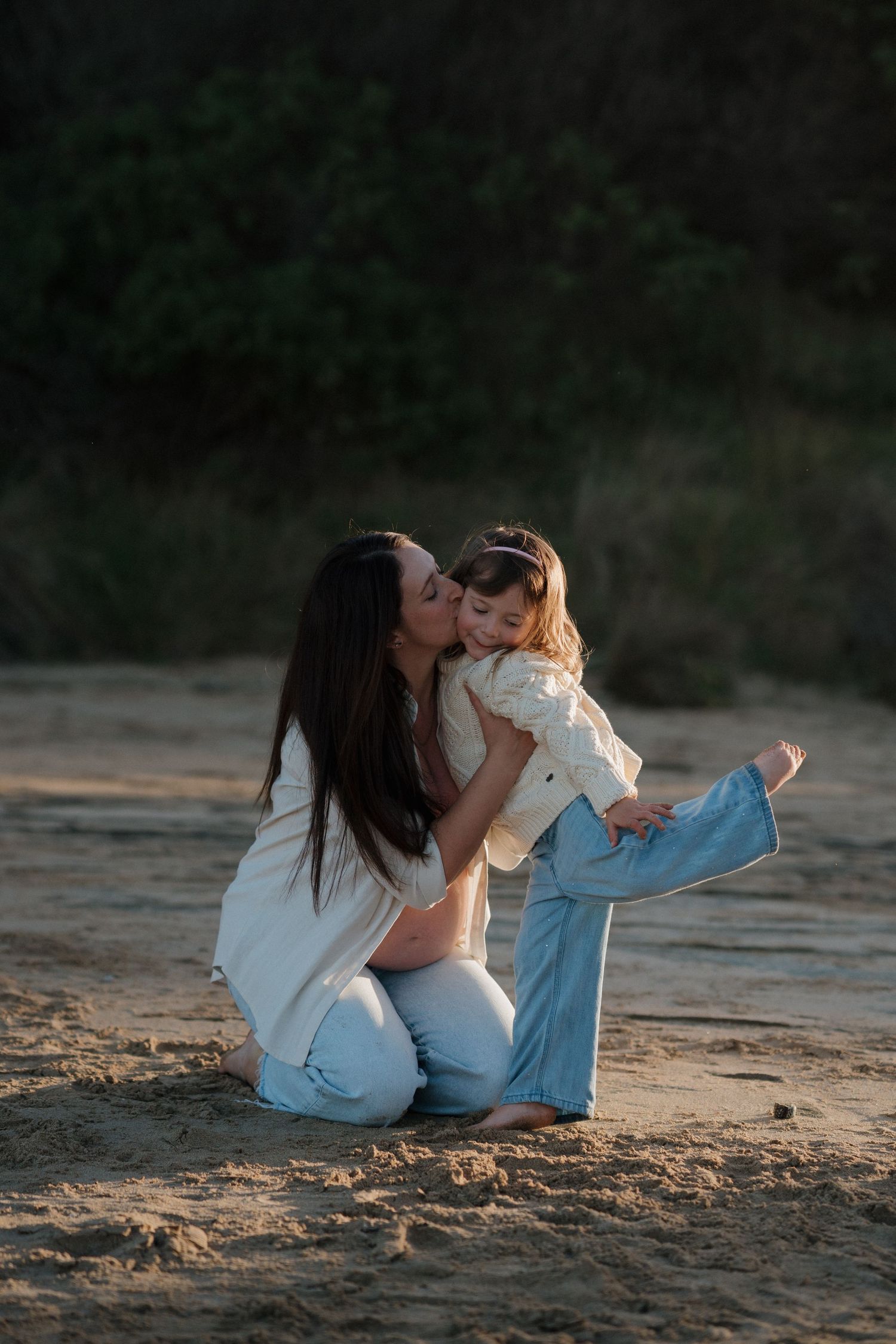 Mother and child sharing tender moments on a sandy beach at sunset in Wye River.