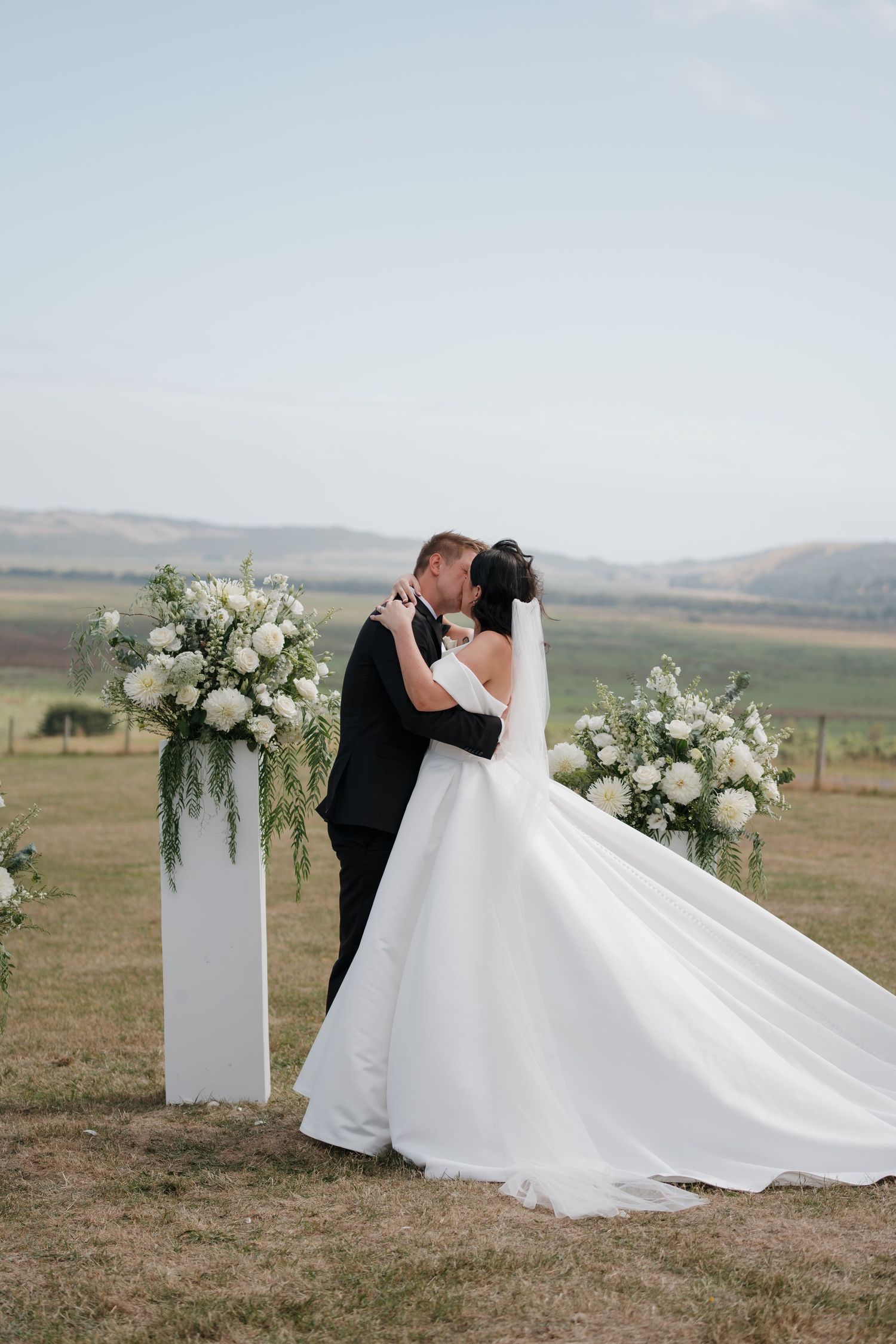 Elegant outdoor wedding ceremony setup with white floral arrangements and flowing dress.