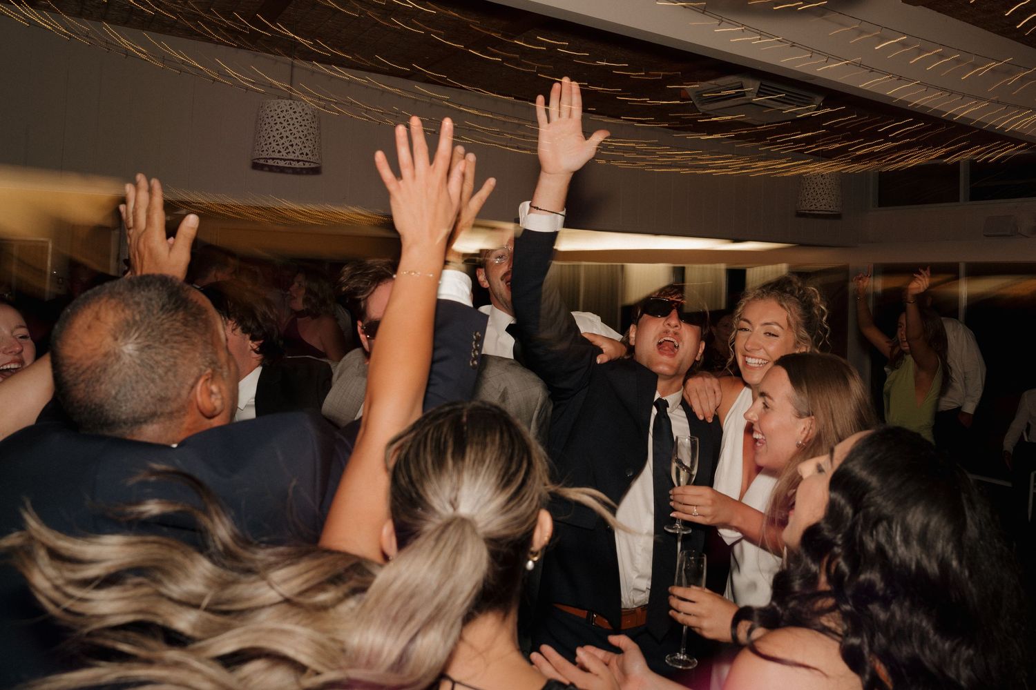 Wedding reception crowd with raised hands dancing and celebrating.