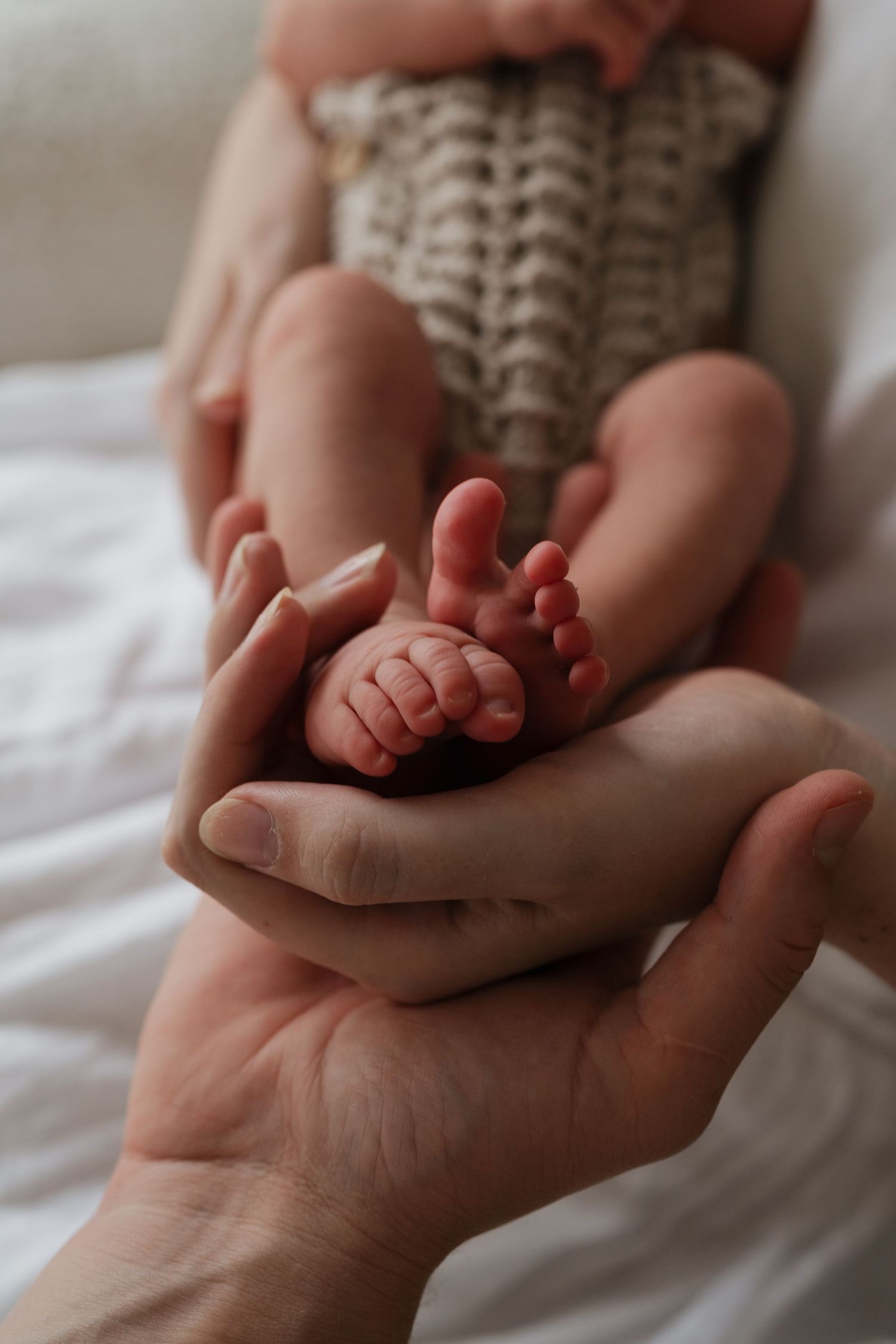 Tiny newborn feet and toes resting in adult hands against white fabric.