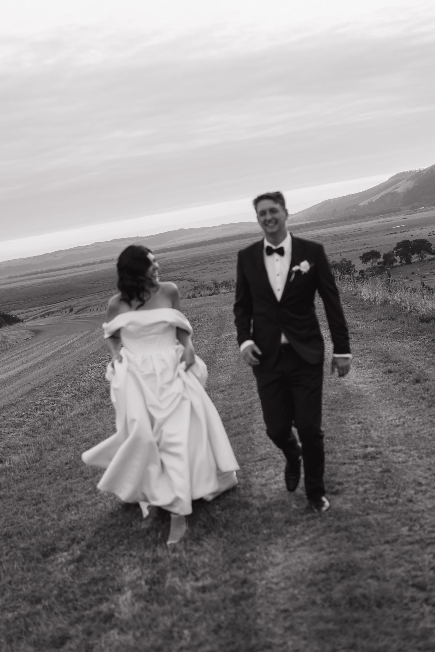 Black and white photo of couple running playfully across a grassy field.