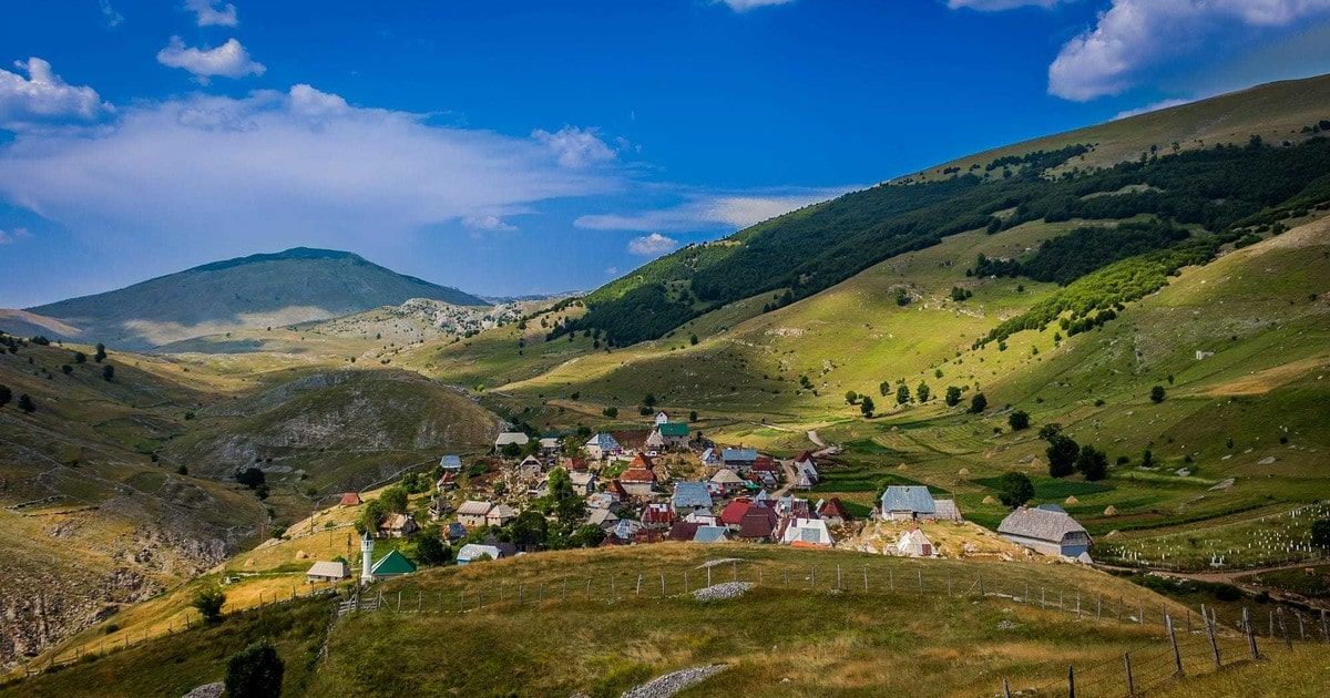 Colorful mountain village nestled in green rolling hills under bright blue sky.