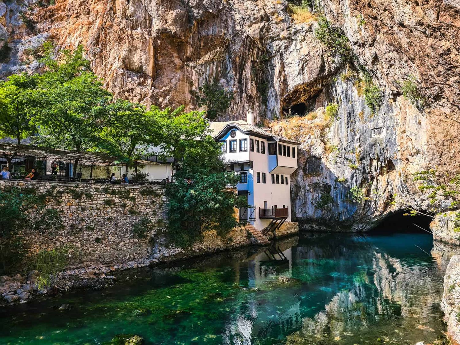 Historic monastery built into cliff face above emerald waters in Bosnia and Herzegovina.