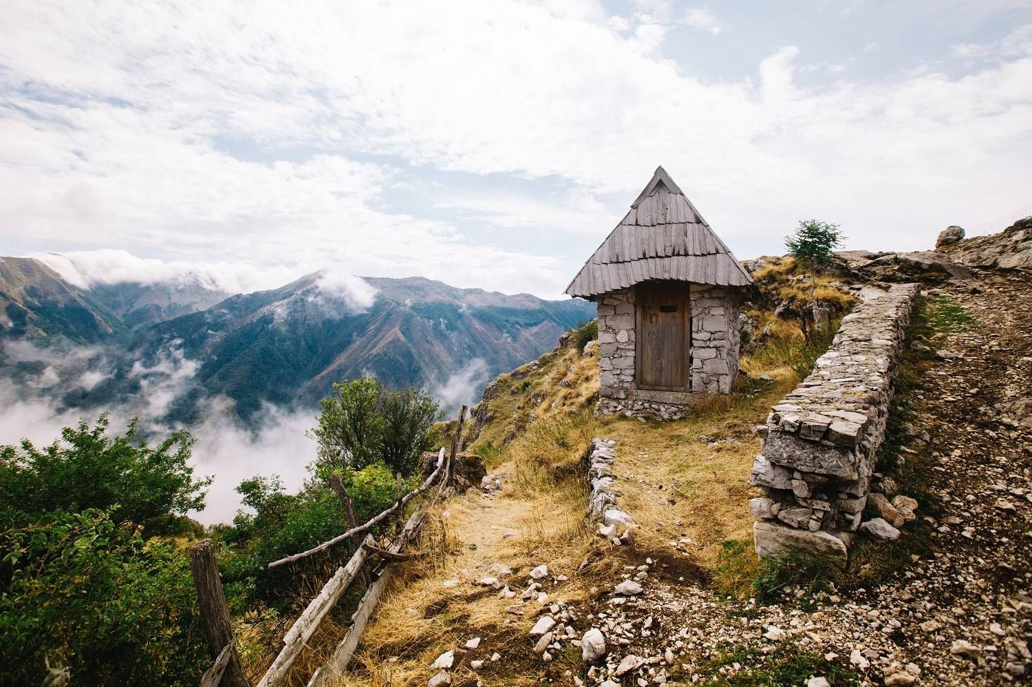 Rustic wooden shelter on mountain ridge with misty peaks and clouds in background.