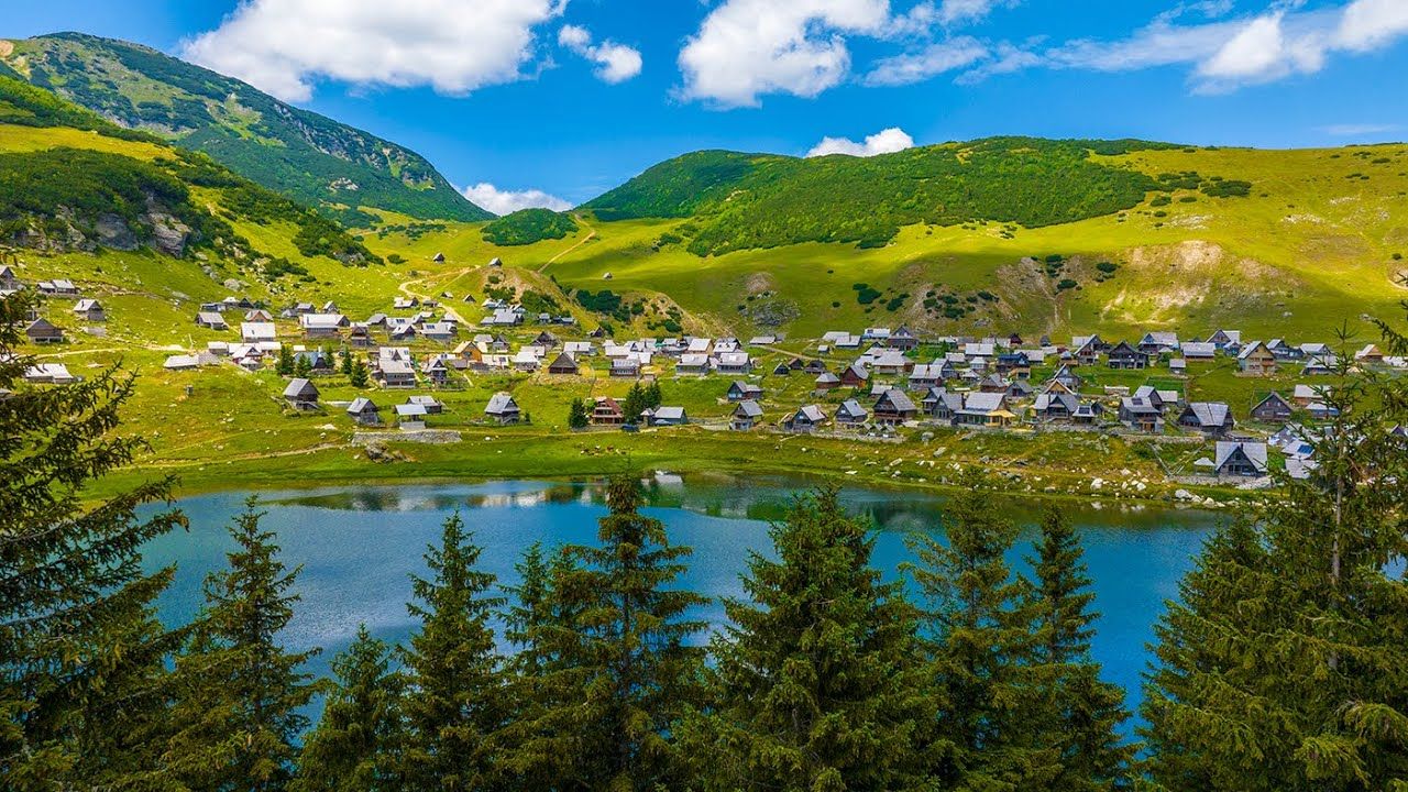 Picturesque mountain village surrounded by lush green peaks and a serene blue lake.