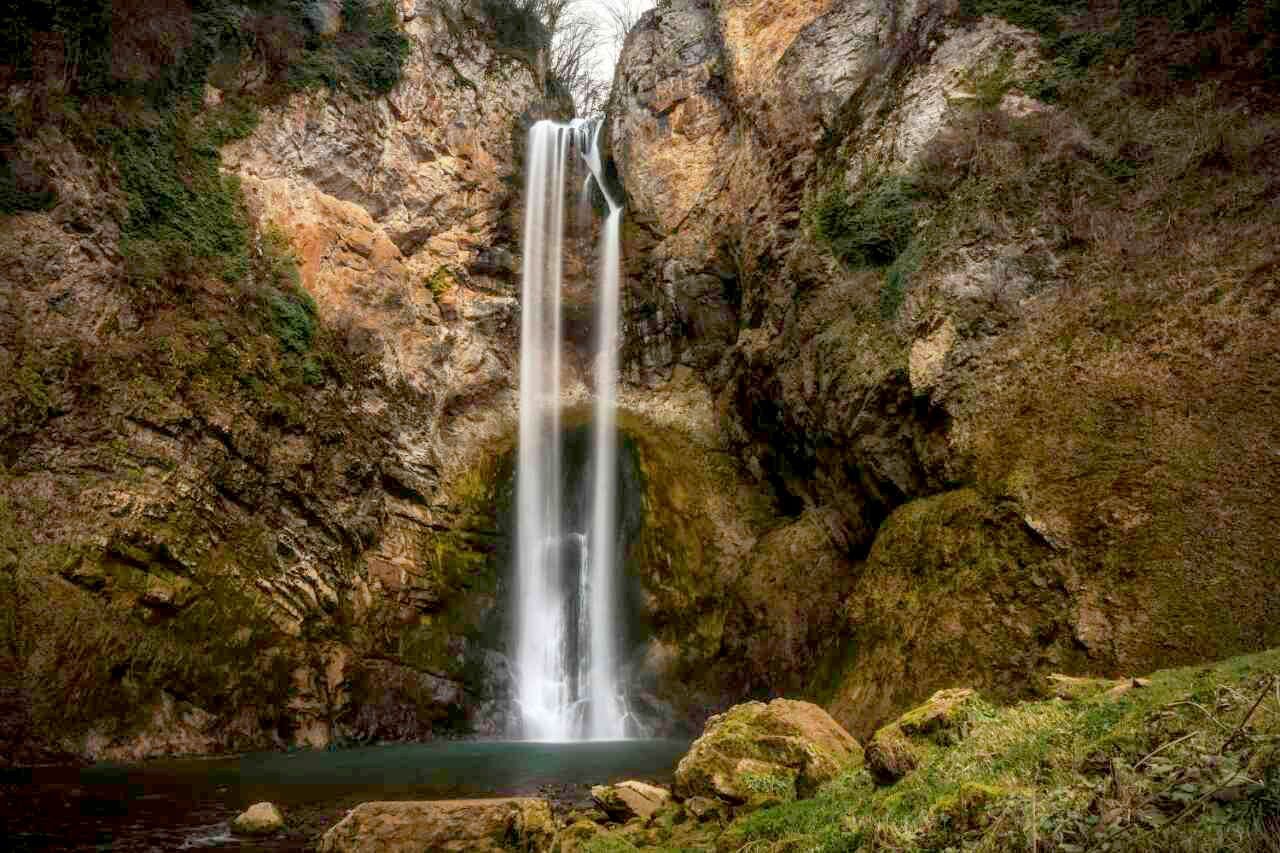 Single stream waterfall plunging dramatically down orange rock canyon walls in natural setting.