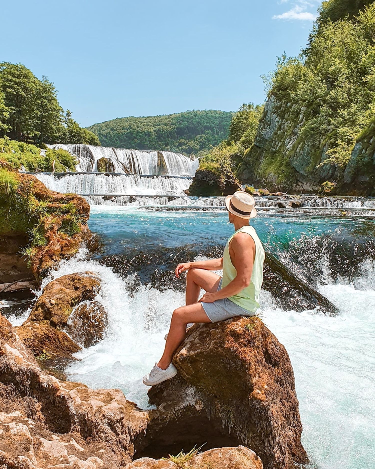 Scenic waterfall view with person sitting on rock enjoying the rushing water and natural landscape.