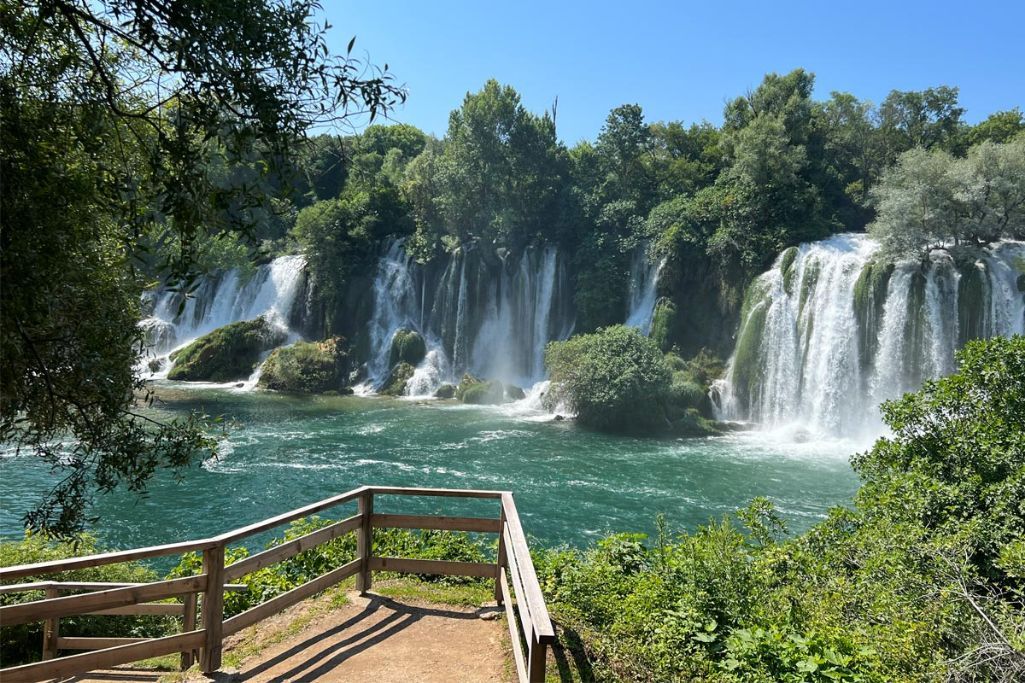 Scenic viewing platform overlooks series of waterfalls cascading into emerald green lagoon.