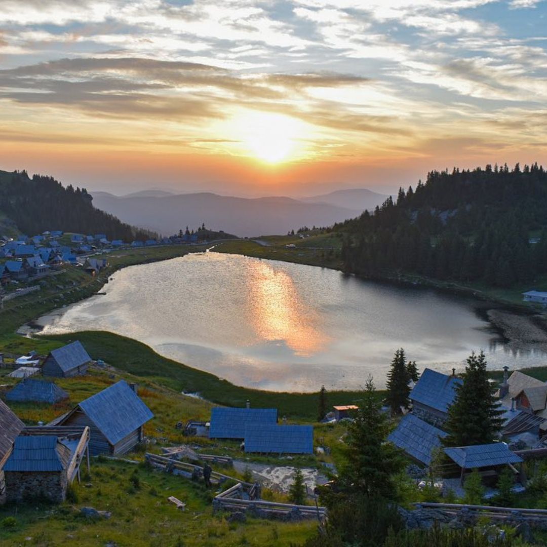 Mountain lake at sunset with blue cabins scattered along shore and golden light reflecting on water.