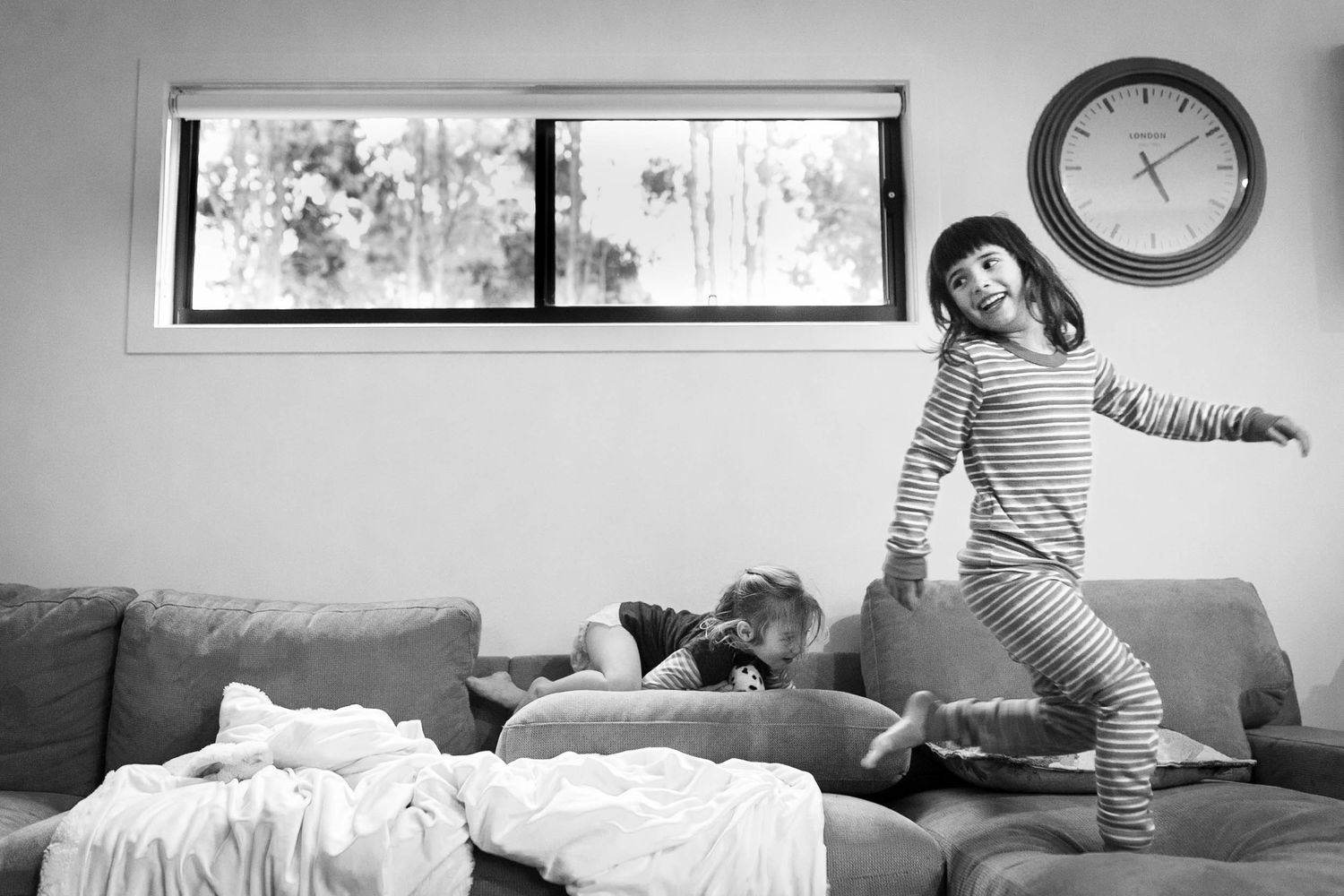 Black and white image showing young person jumping on a couch indoors.