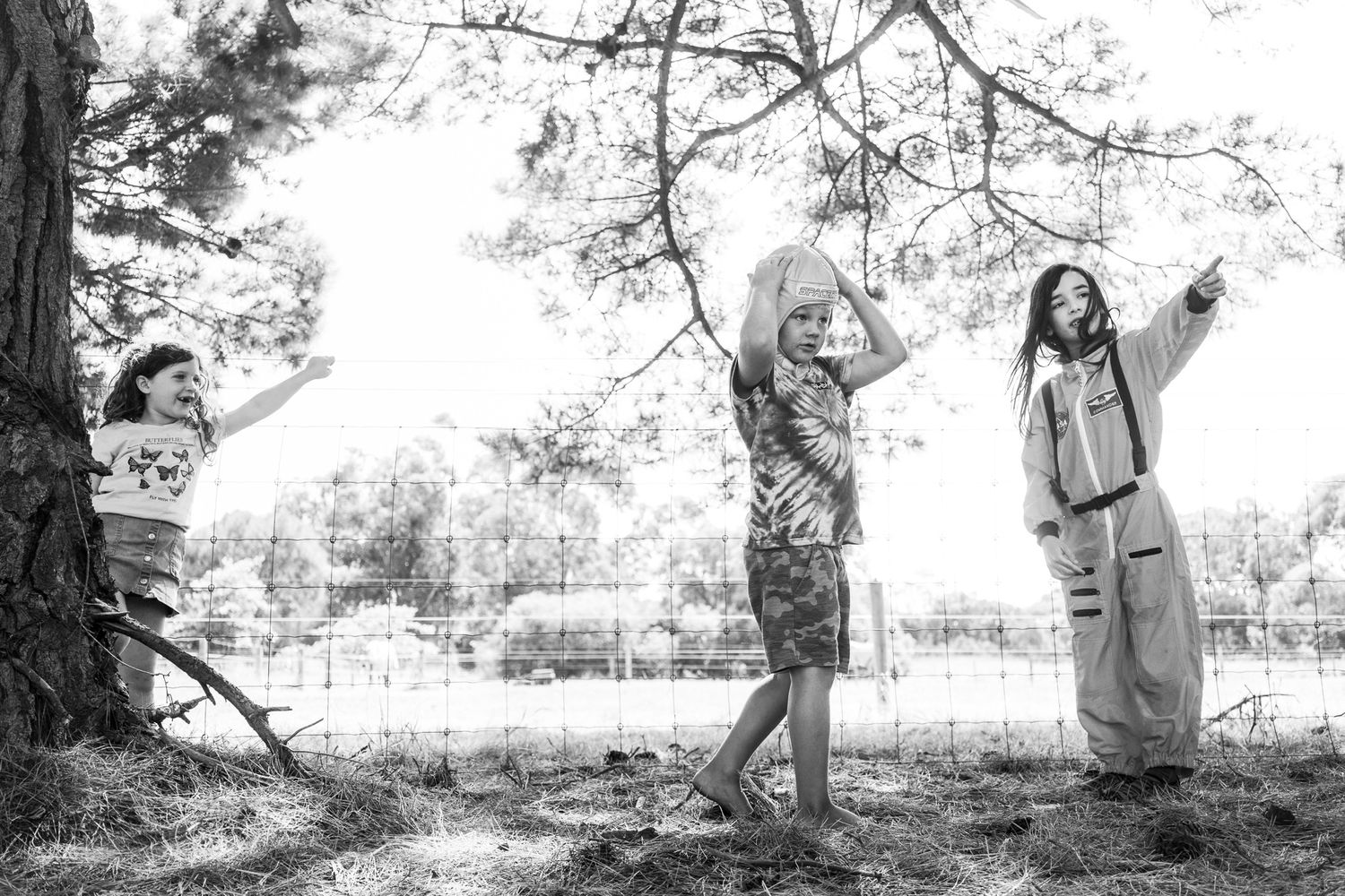 Three people enjoy a playful moment outdoors in a park setting captured in black and white photography.