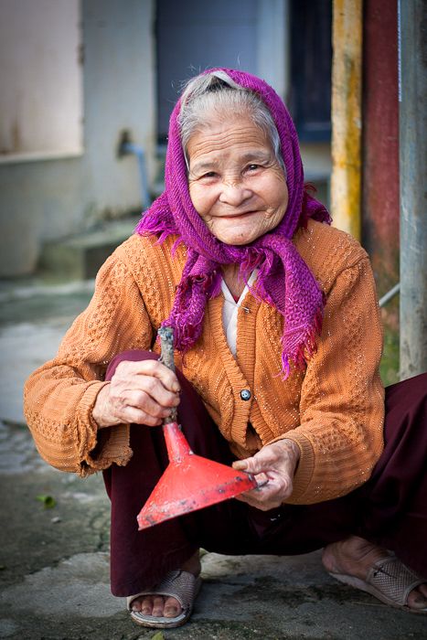 A portrait of an elderly person in orange sweater and purple headscarf expressing joy.