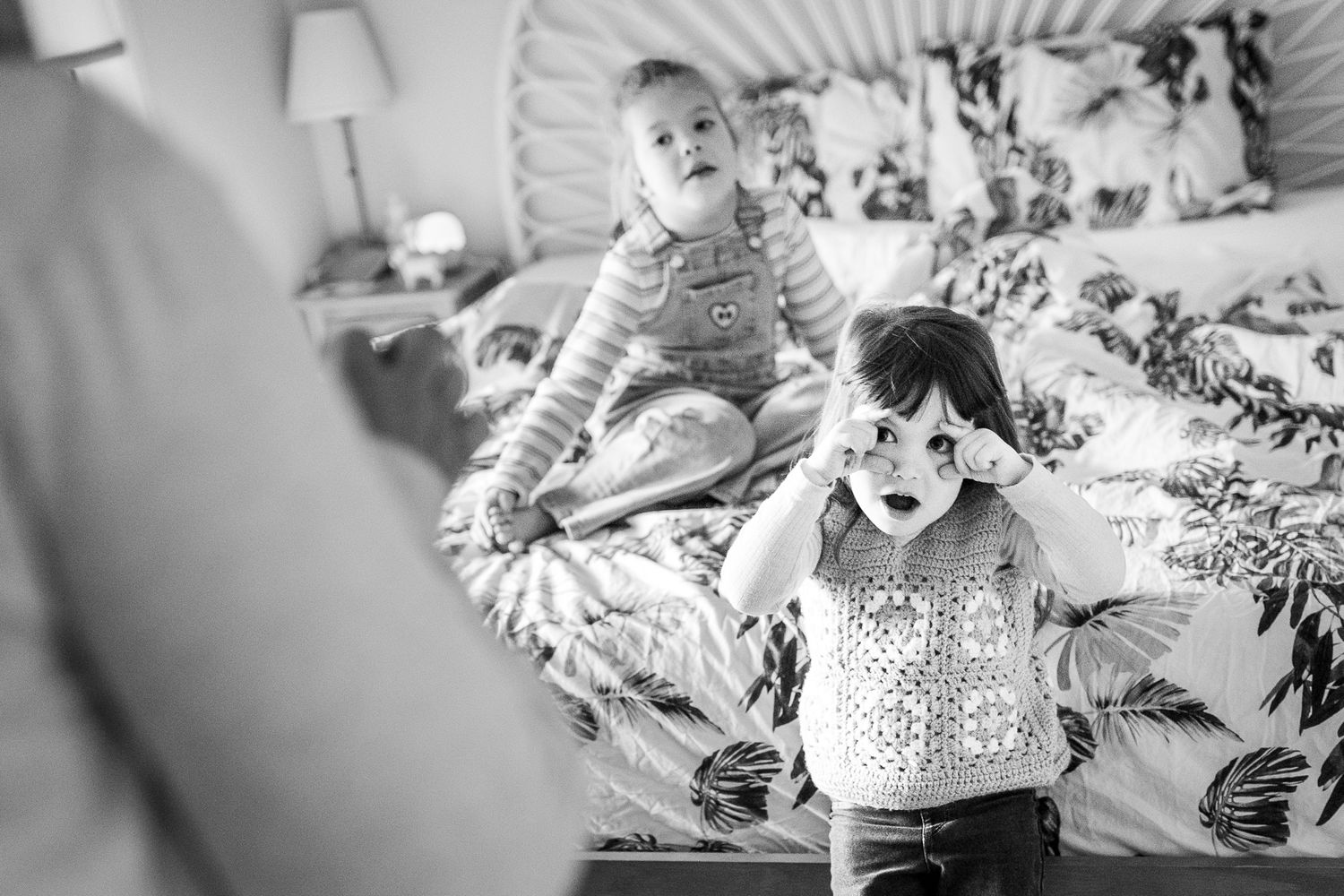 Black and white photograph capturing playful indoor moment between children and parent in a bright room.