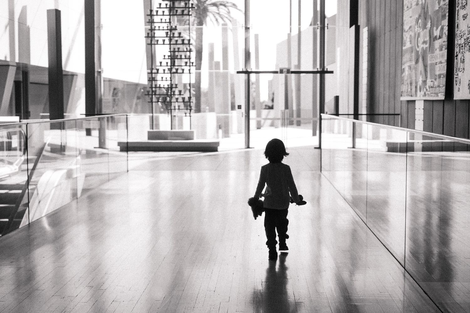 A silhouette of a person walks through a bright modern hallway with glass walls and reflective floors.