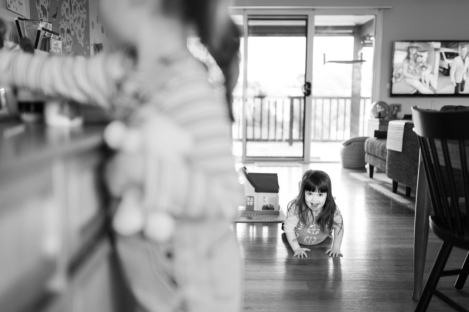 A black and white photograph showing interior spaces with natural light streaming through windows and a young child playing.