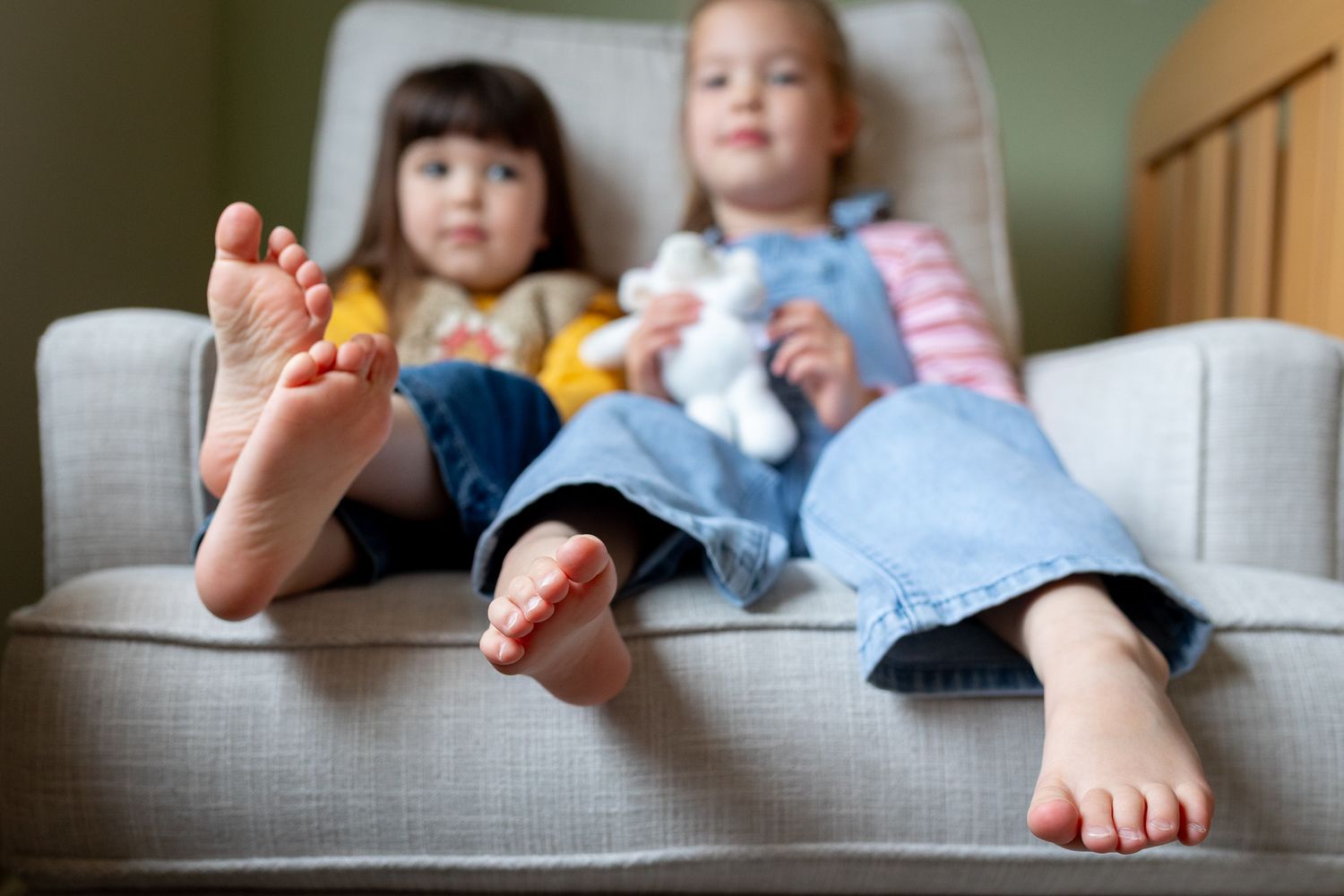 Close-up view of small feet resting on a gray couch cushion in natural light.