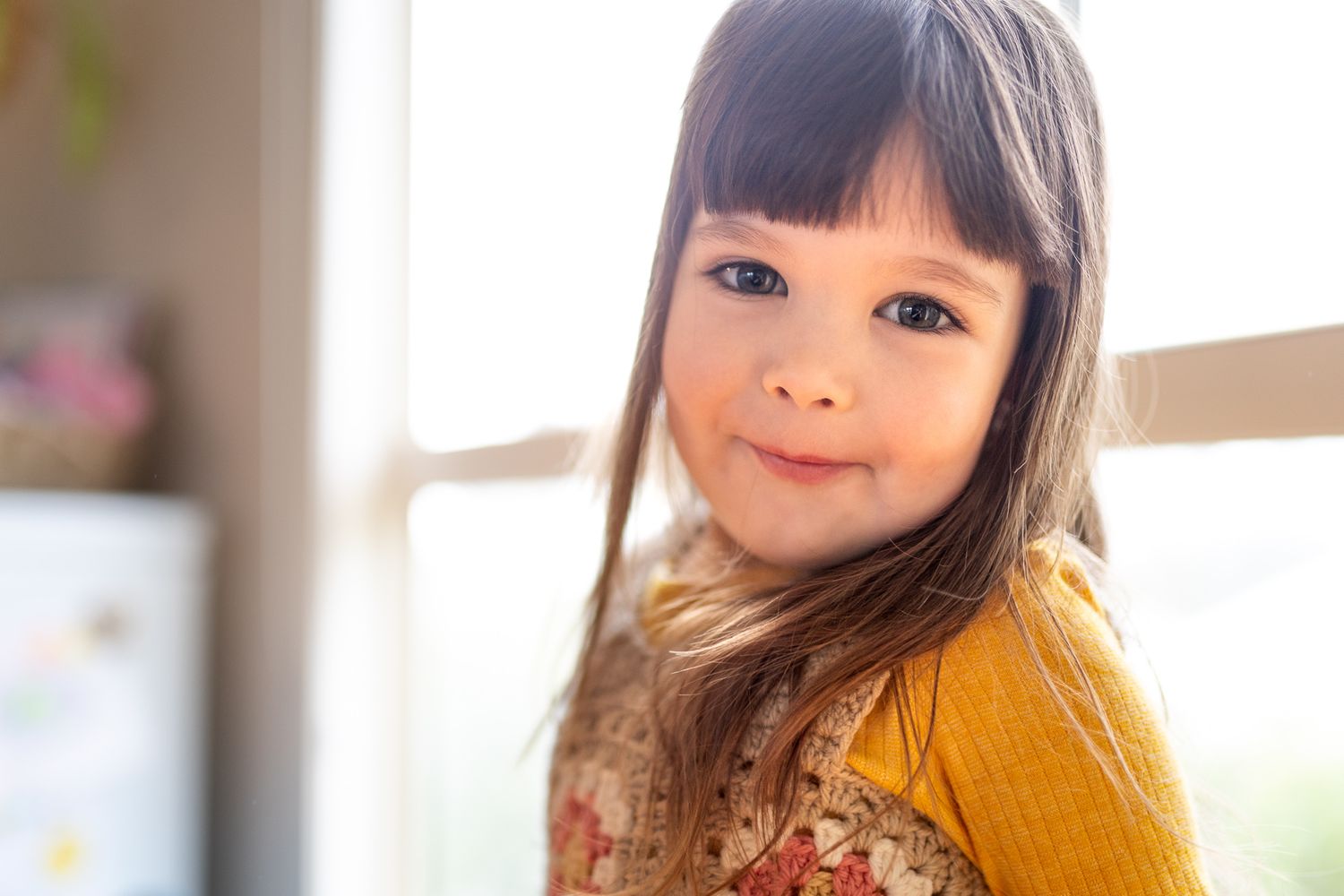 Child in yellow sweater by window with soft natural lighting.