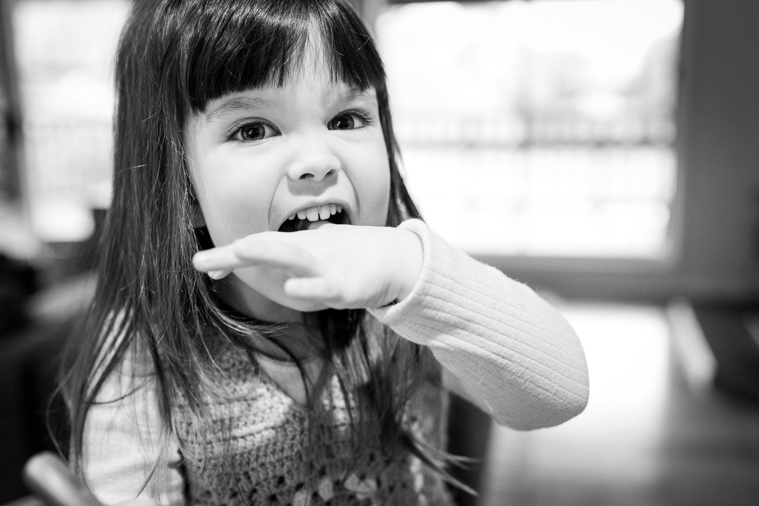 Black and white photo of a child capturing playful expression as she licks her fingers.