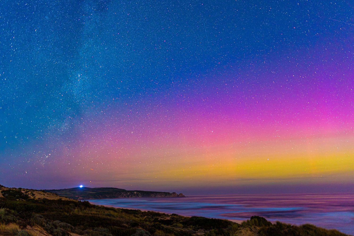 Stunning aurora australis displays vibrant colours across night sky over coastal landscape.