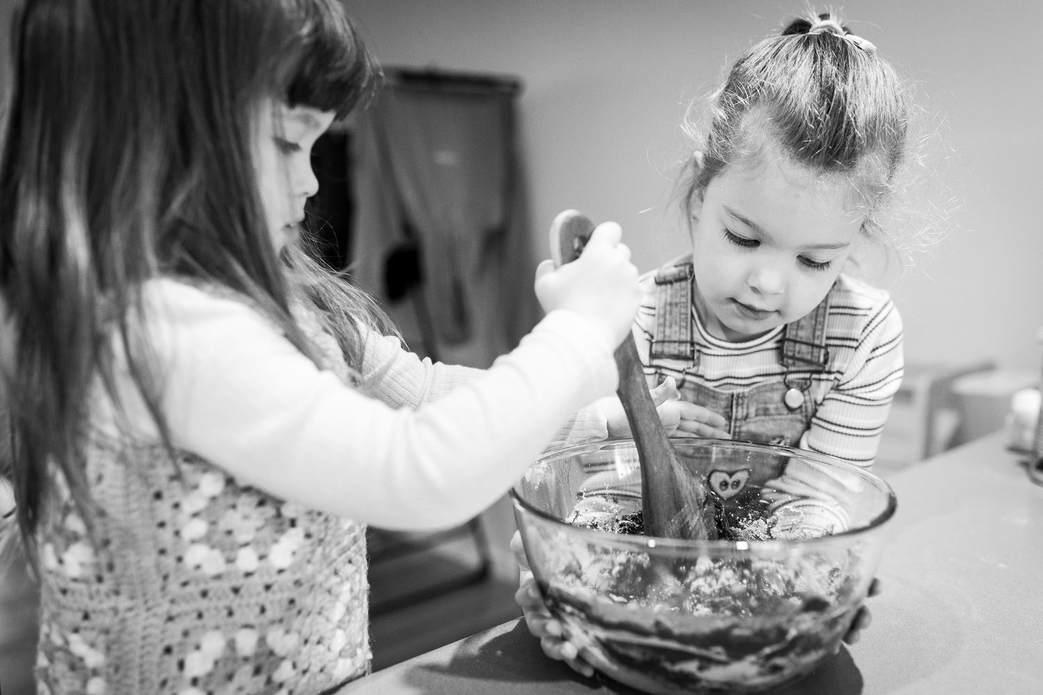 Black and white photo depicting gentle moment between siblings baking together in a home setting.
