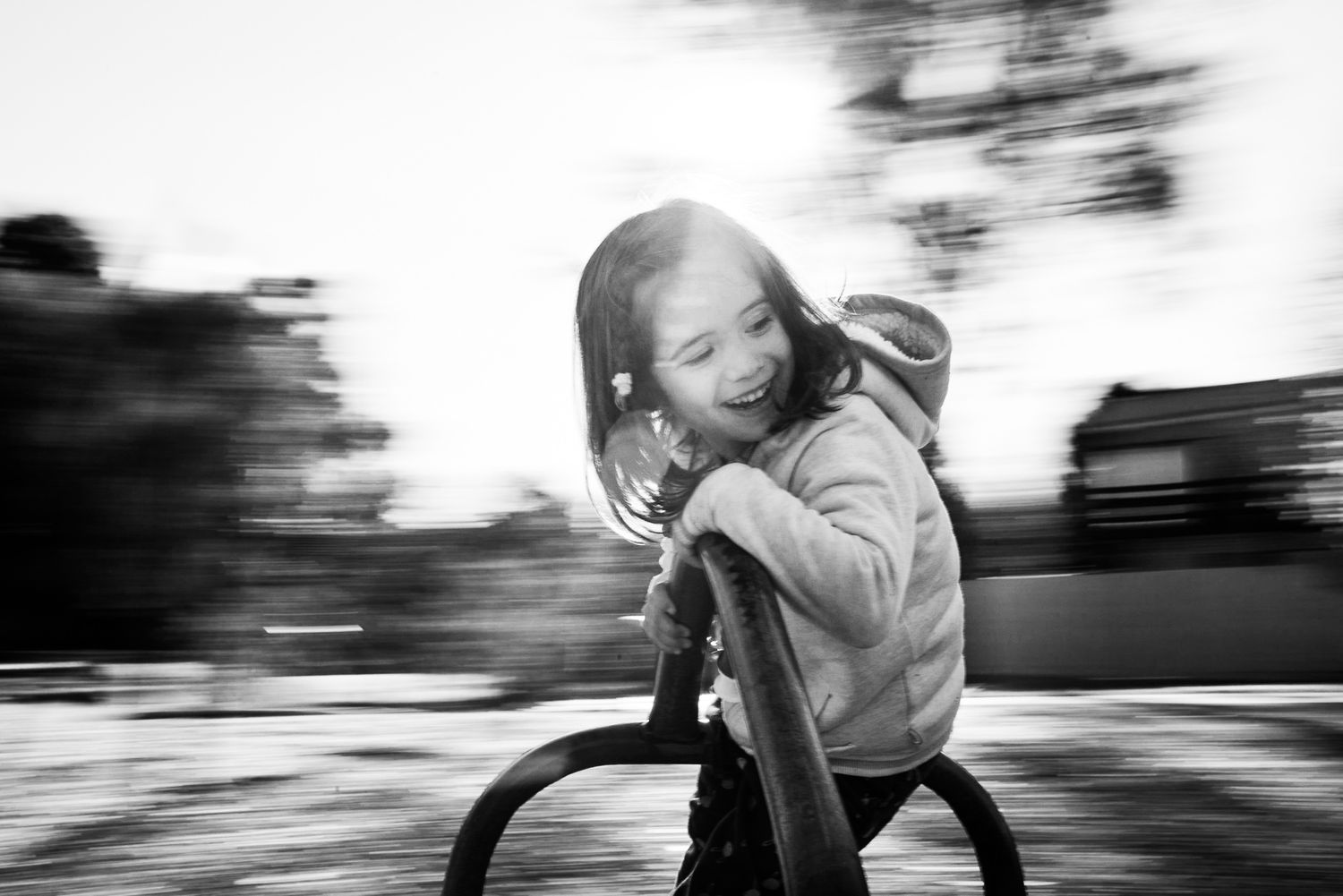 A child spins joyfully on playground equipment in black and white motion blur photography.
