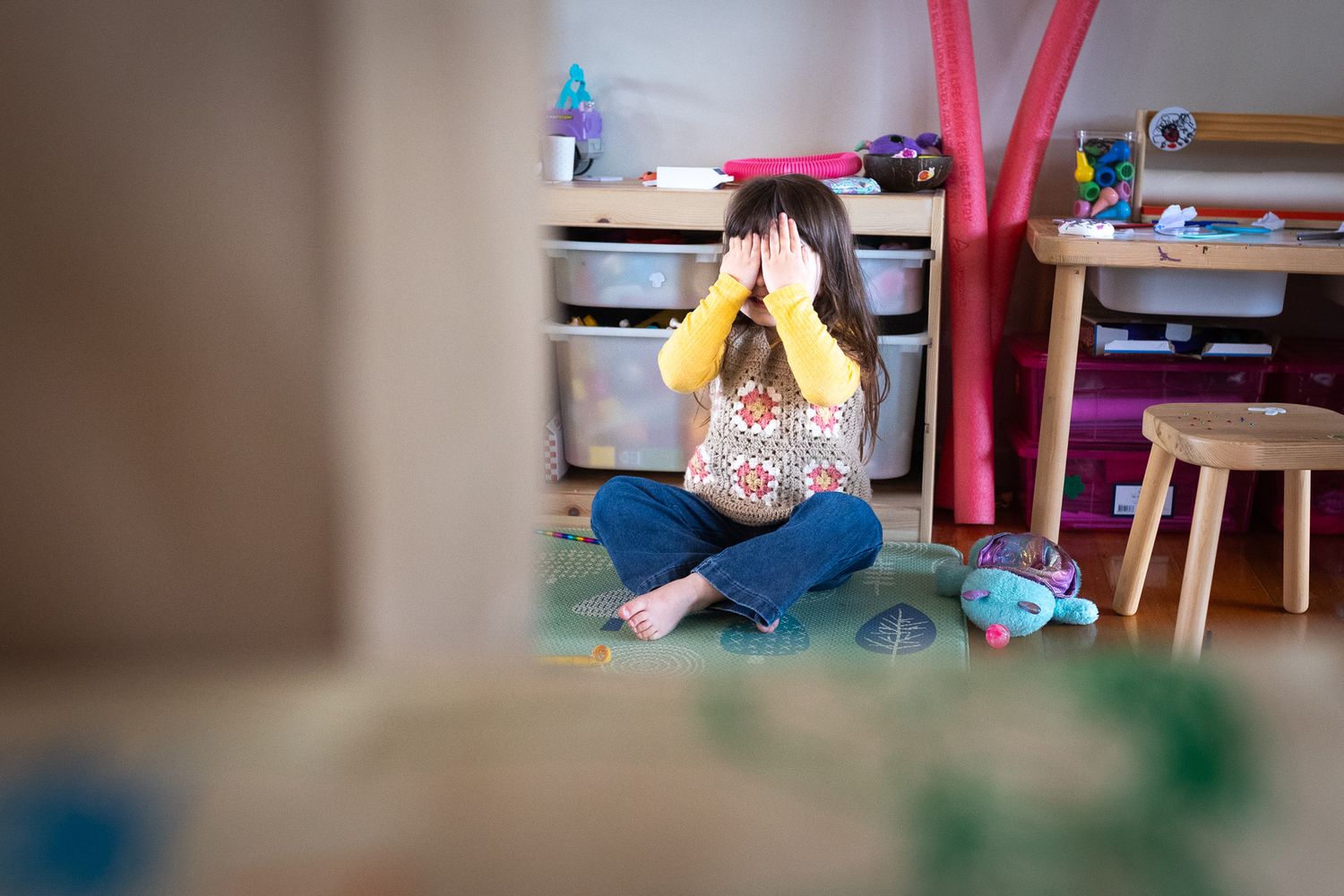 Colorful playroom setting and young child playing hide and seek with toys and furniture visible.