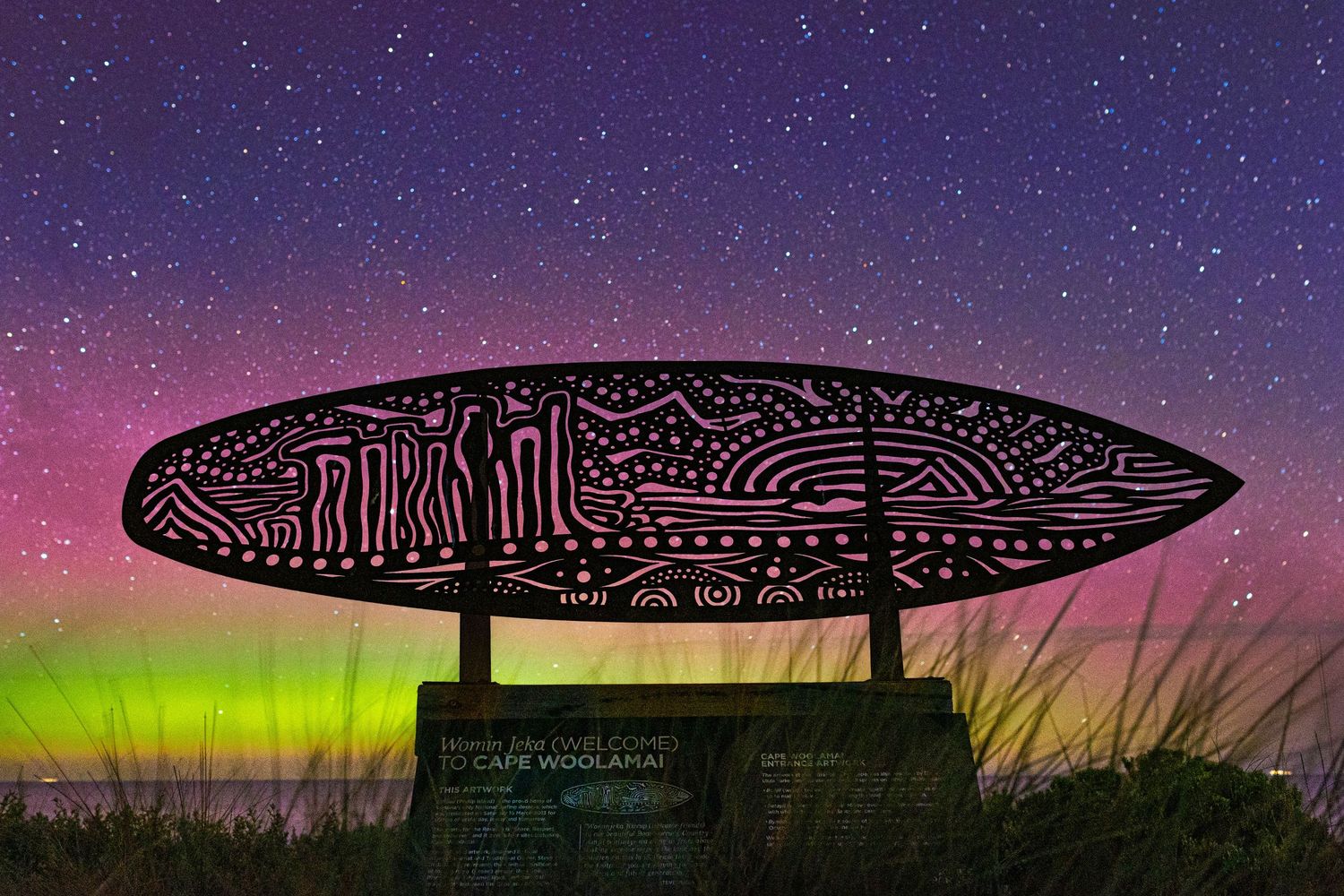 Silhouetted architectural surfboard structure against a colourful aurora australis southern lights sky.