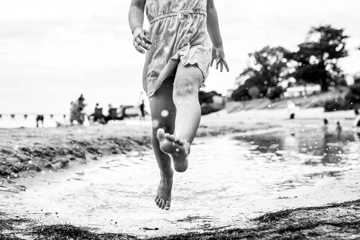 Black and white image of feet running along a sandy beach.