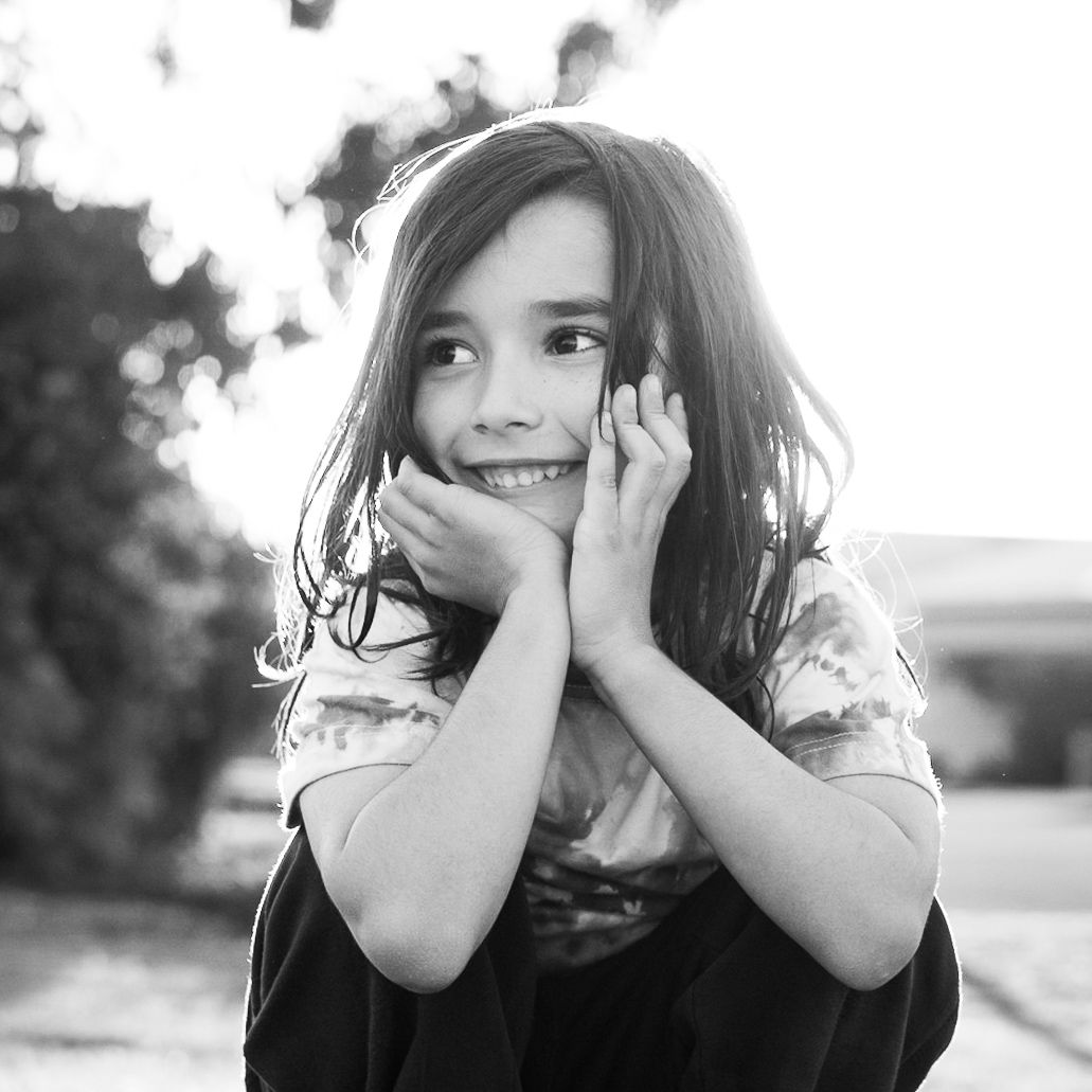 A black and white portrait series shows a child making playful expressions while covering their face with hands.