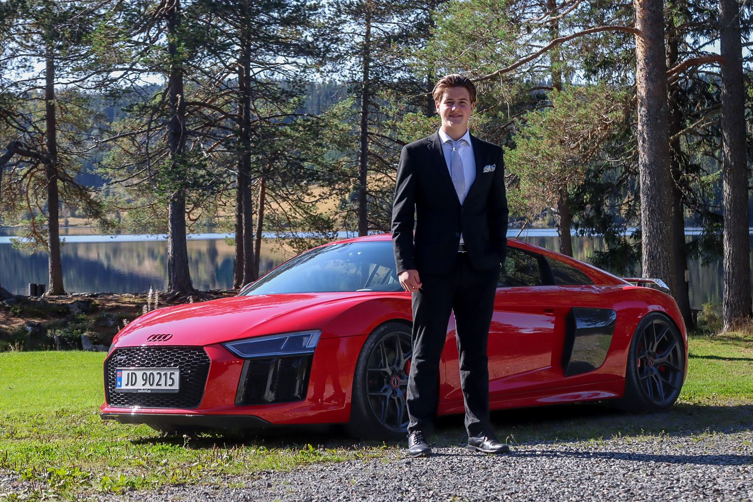 Konfirmant i mørk dress fotografert med en rød Audi R8 ved Skumsjøen i Gjøvik.