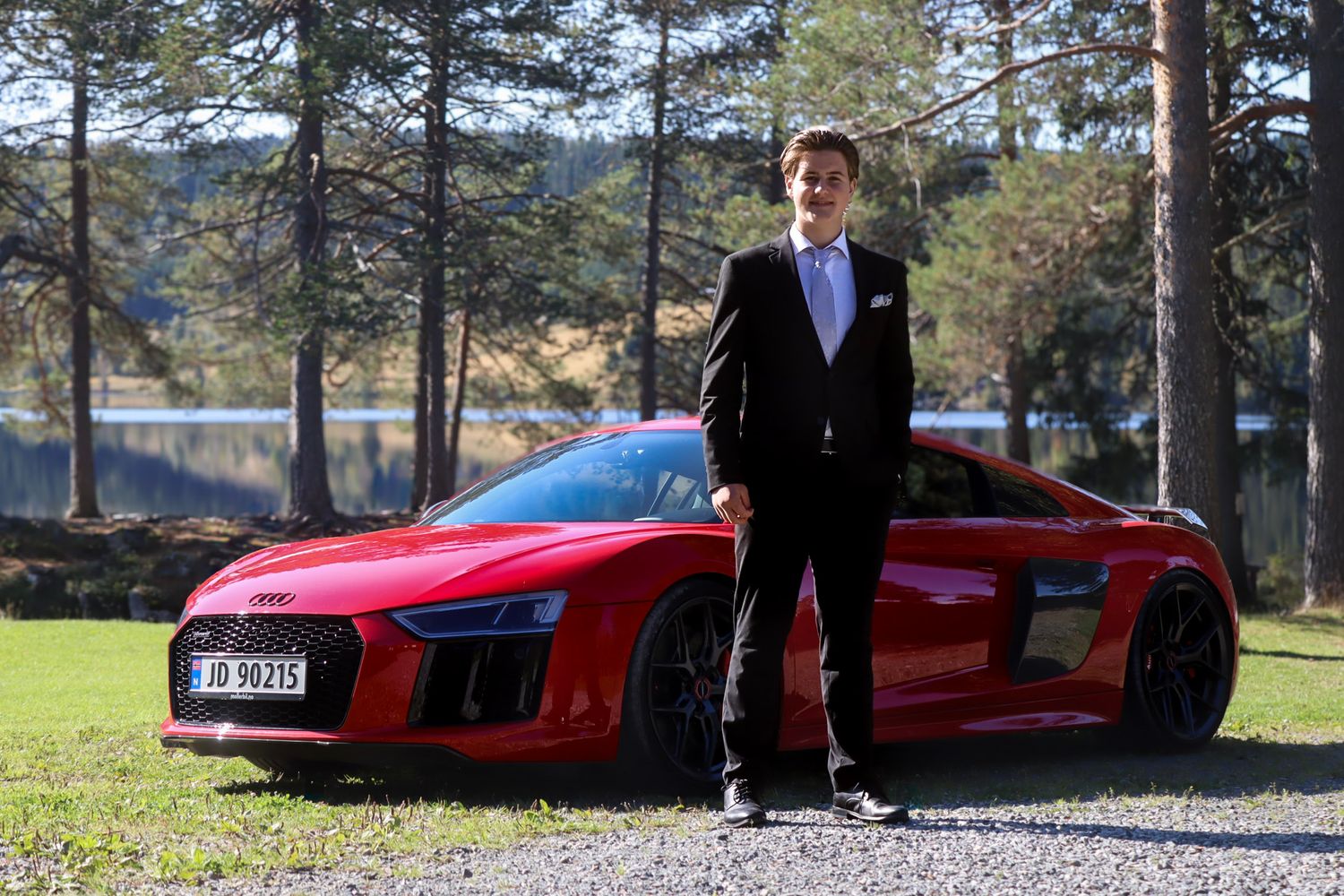 Konfirmant i svart dress fotografert med en rød Audi R8 ved Skumsjøen i Gjøvik.