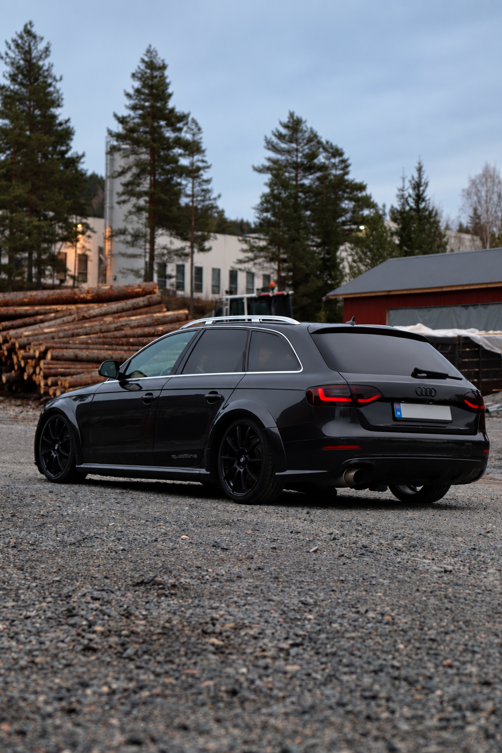 Svart Audi A4 fotografert på grusvei med furutrær og tømmerstokker i bakgrunnen.