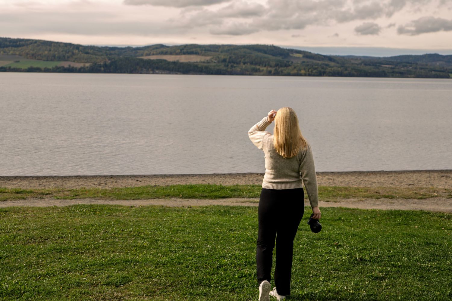 Fotograf Amalie fra Photo by Rime stående ved vannet med kamera på en overskyet dag.