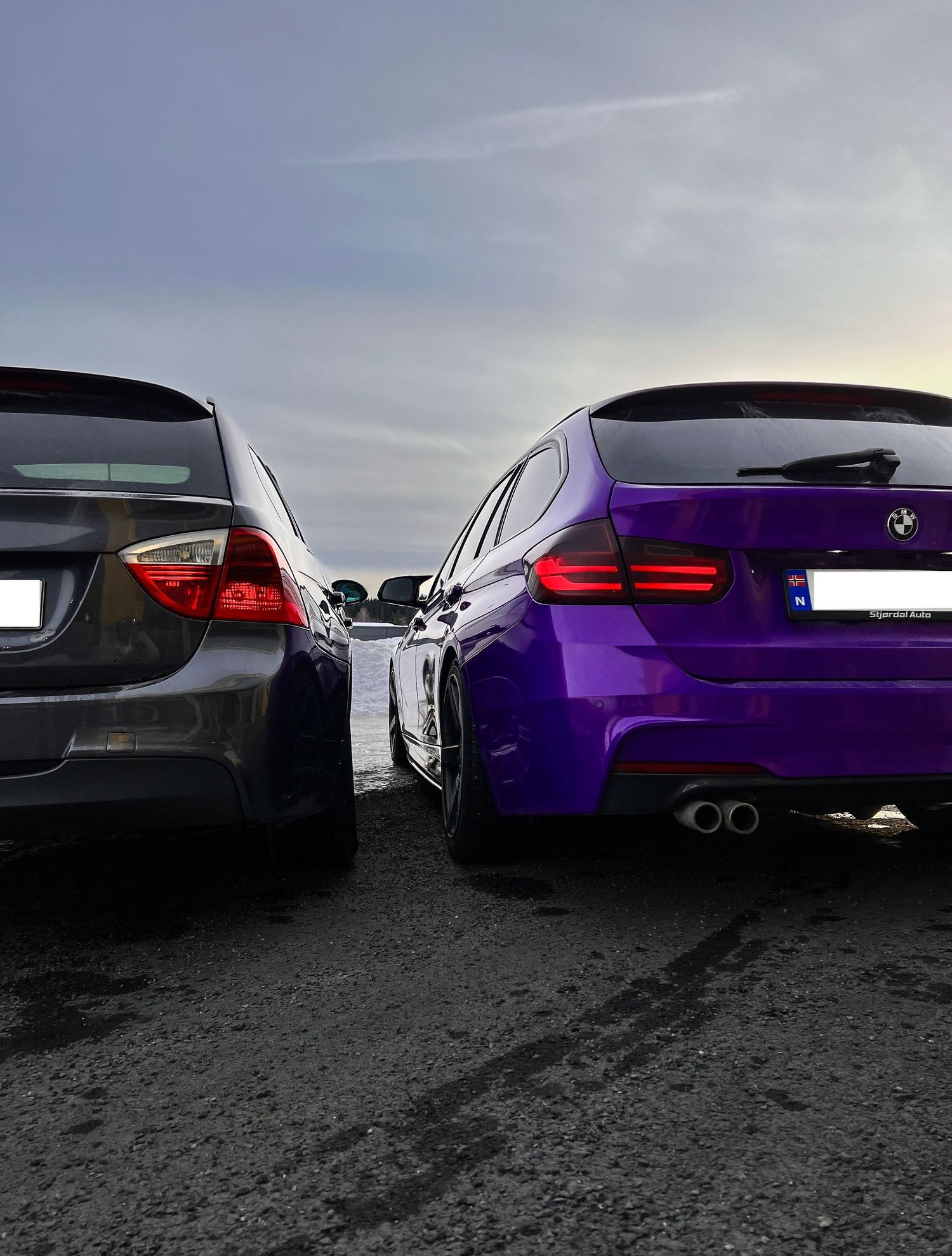 To BMW-er, én mørkegrå og én lilla, fotografert bakfra i skumringen.