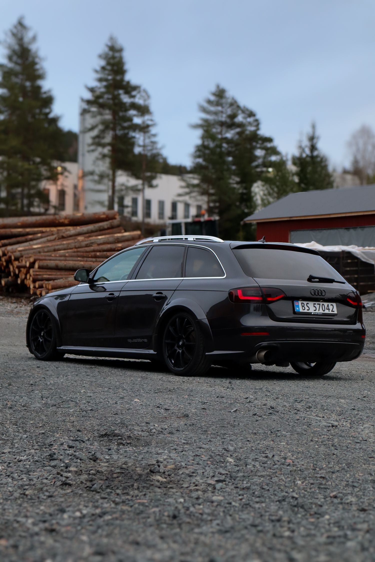 Svart Audi A4 fotografert på grus med tømmerstokker og skog i bakgrunnen.