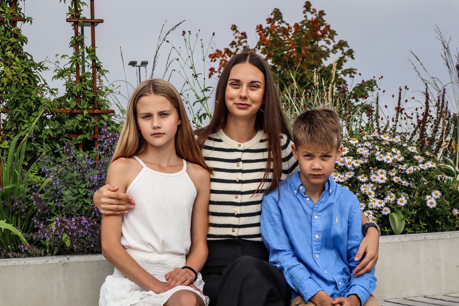 Mor fotografert sammen med sønnen og datteren foran blomster i Mjøsparken.