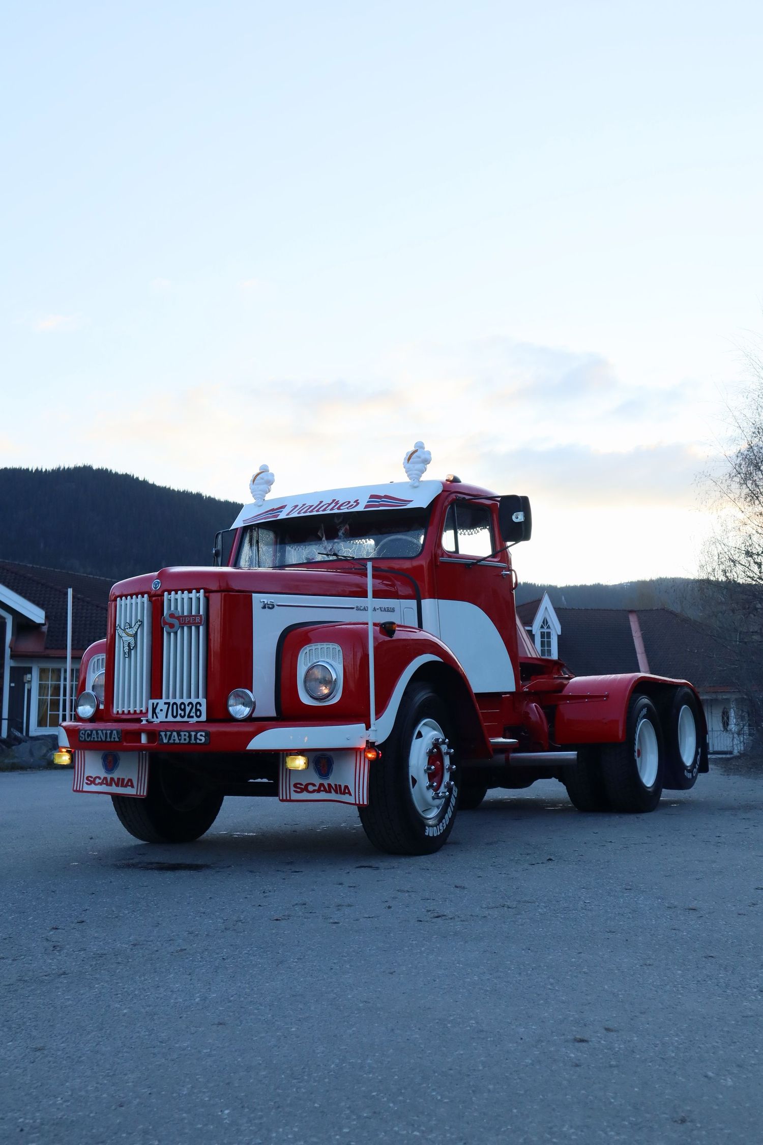 Klassisk rød og hvit Scania-Vabis lastebil fotografert i skumringen med fjell i bakgrunnen.